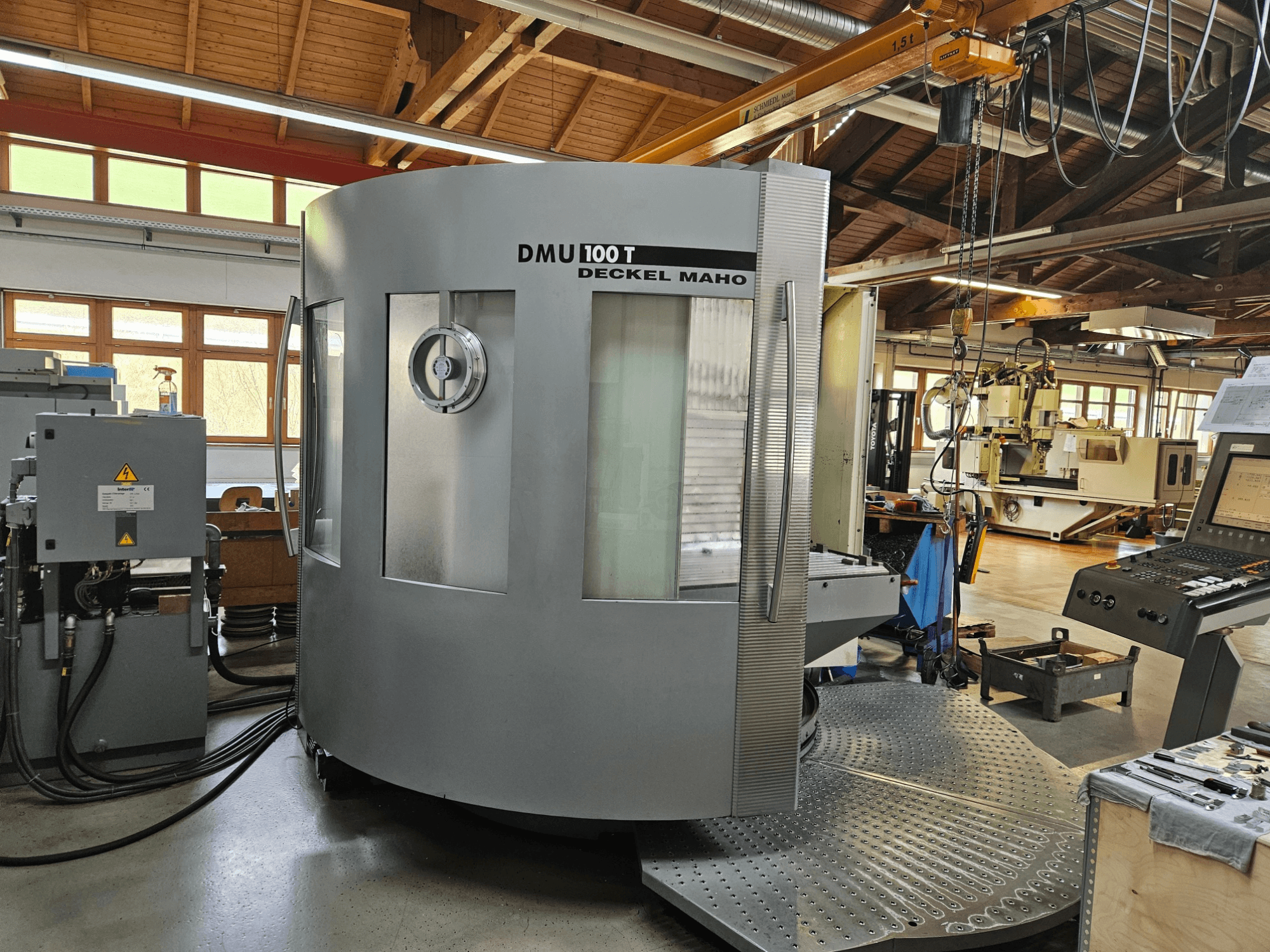 DMU 100 T Deckel Maho CNC machine viewed from the front, featuring a large circular base, control panel, and glass enclosure.