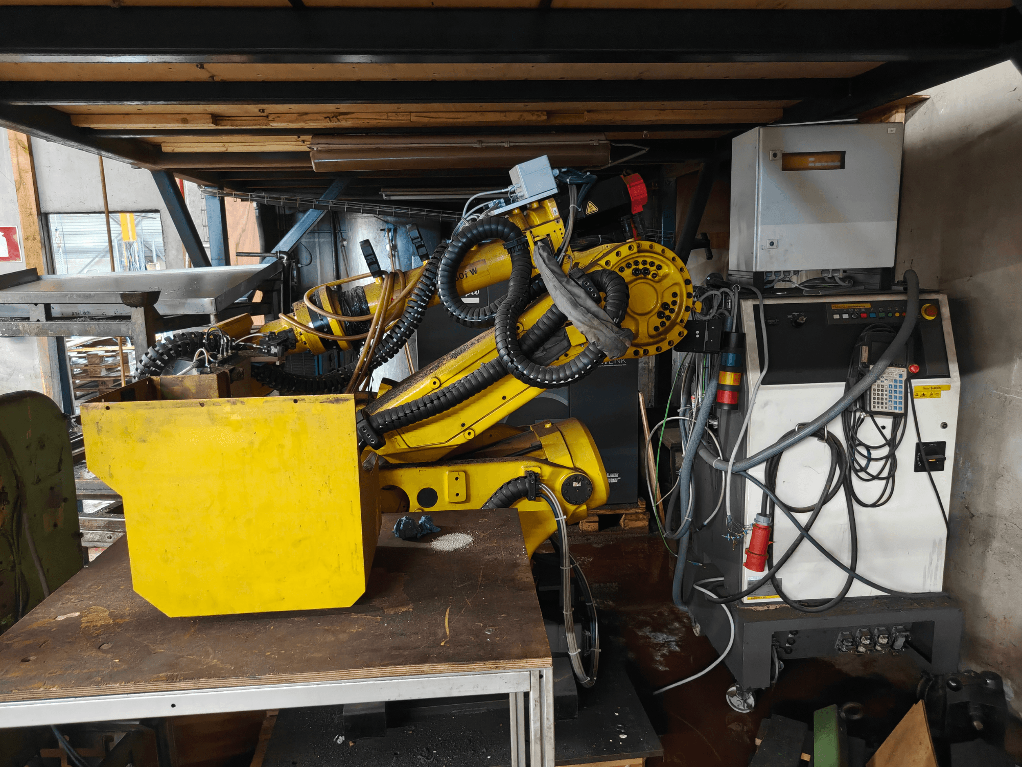 Front view of a FANUC Robot S-430i W arm, yellow with control panel, cables, and a yellow component on a workbench.