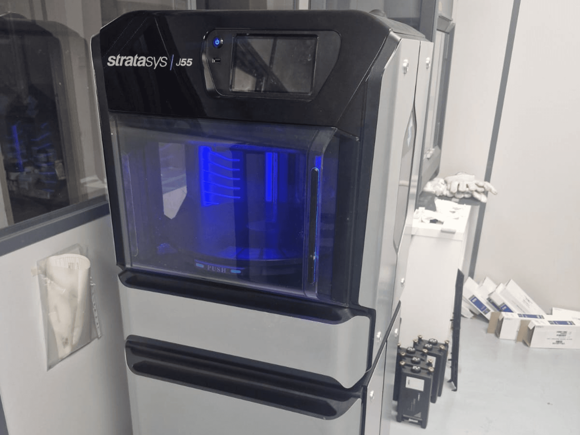Stratasys J55 Prime plastic 3D printer in a side view, showcasing its sleek design and illuminated printing area.