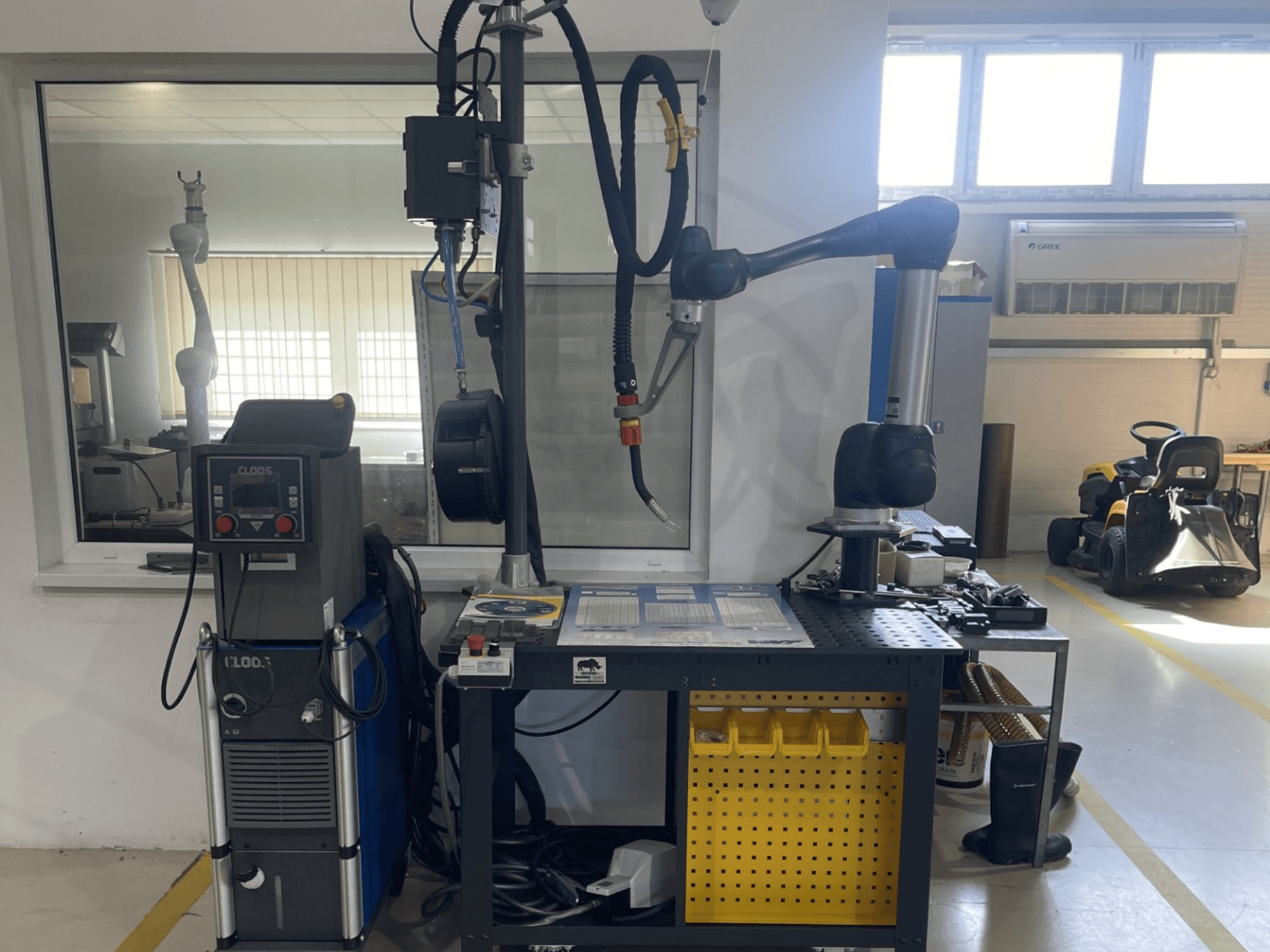 DOOSAN M1013 collaborative robot in a workshop, side view with welding equipment and tools on a workbench.