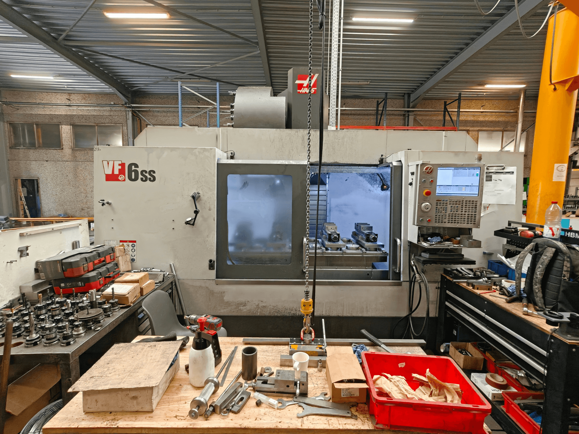 Haas VF-6SS vertical machining center in a workshop, side view showcasing control panel and workspace clutter with tools.