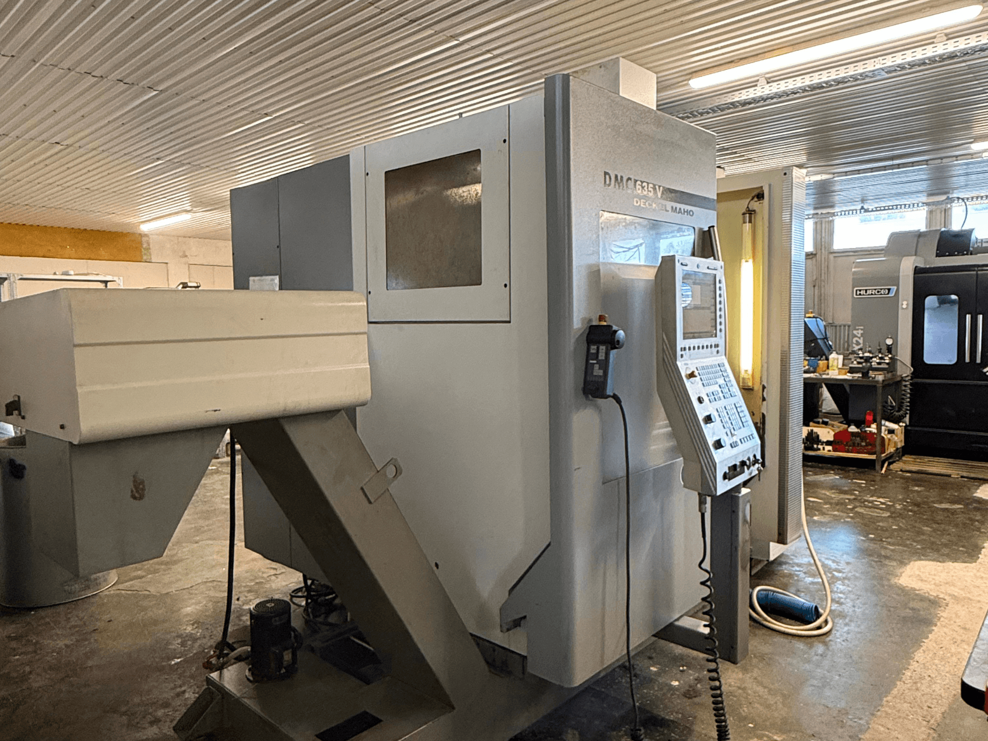 DMC G635V milling machine in a workshop, front view with control panel and connected power tools visible.