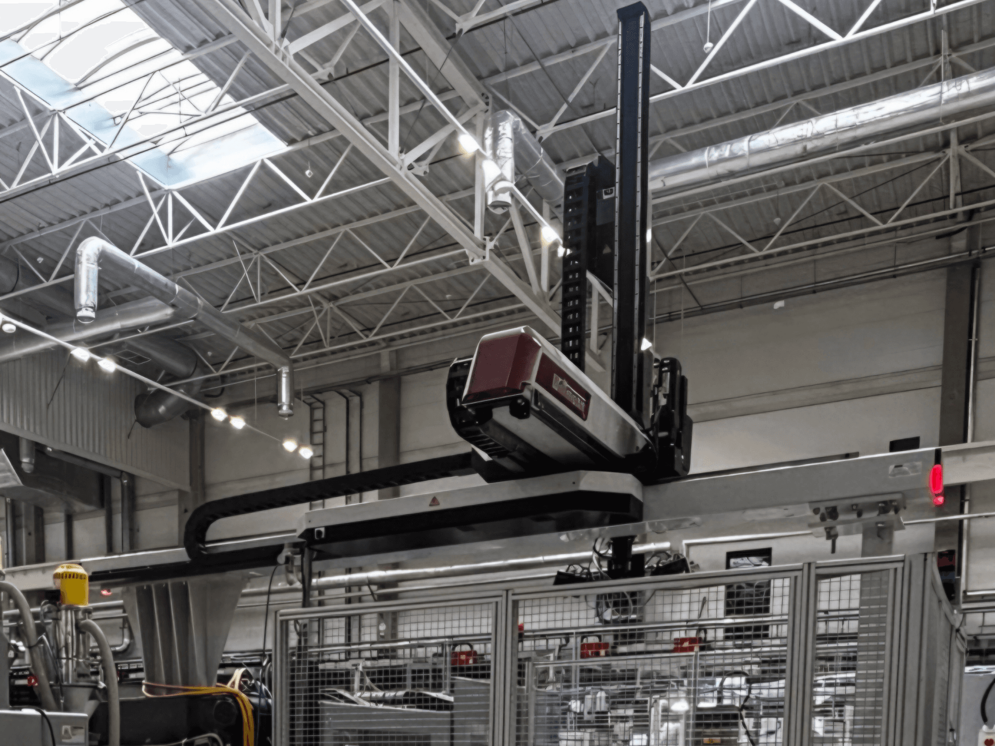 WITTMANN W832PRO plastic processing machine in a factory setting, side view showcasing the overhead system and industrial background.