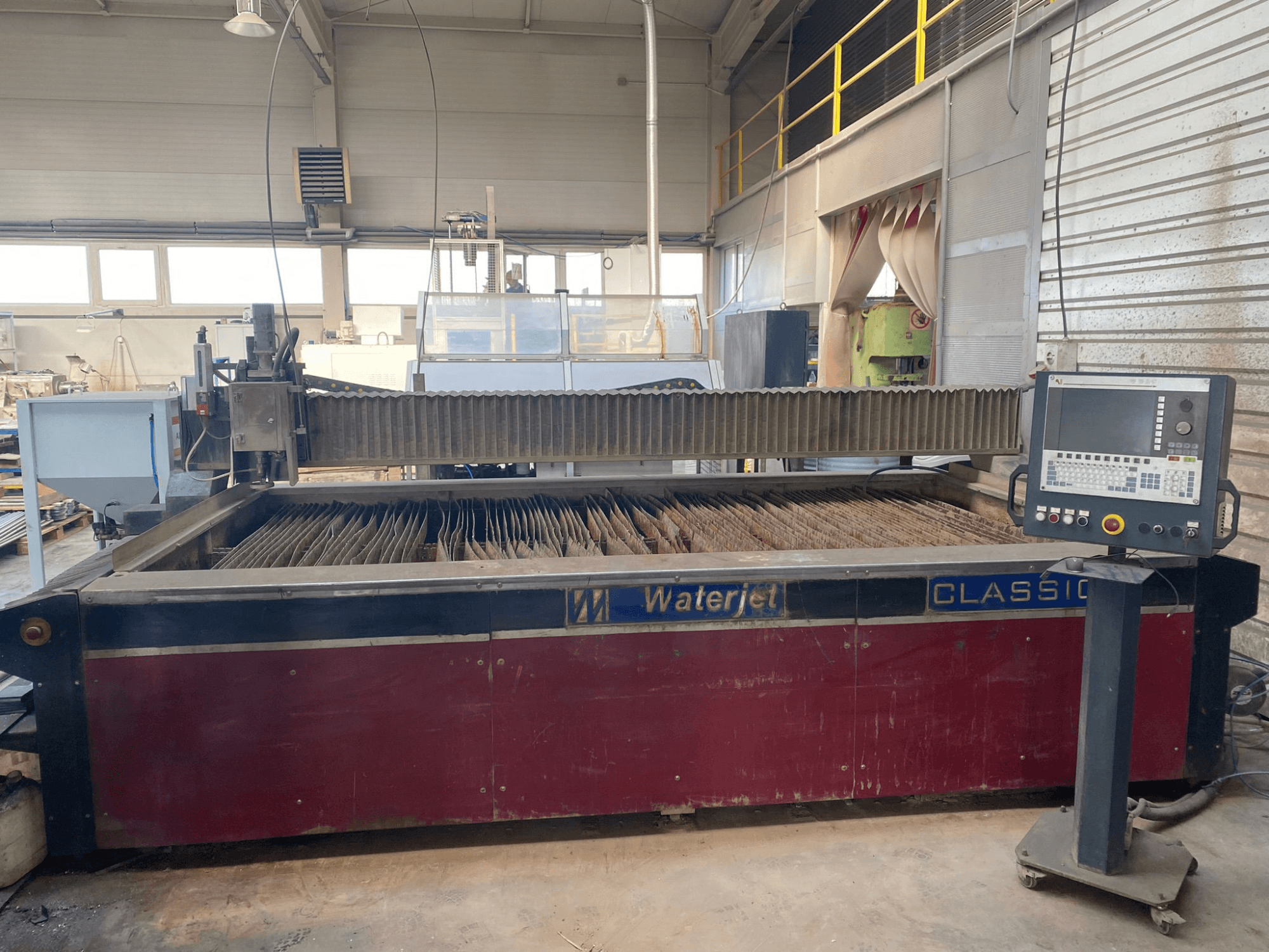 Waterjet cutting machine CLASSIC, front view, showing water tank, control panel, and multiple metal cutting heads inside.
