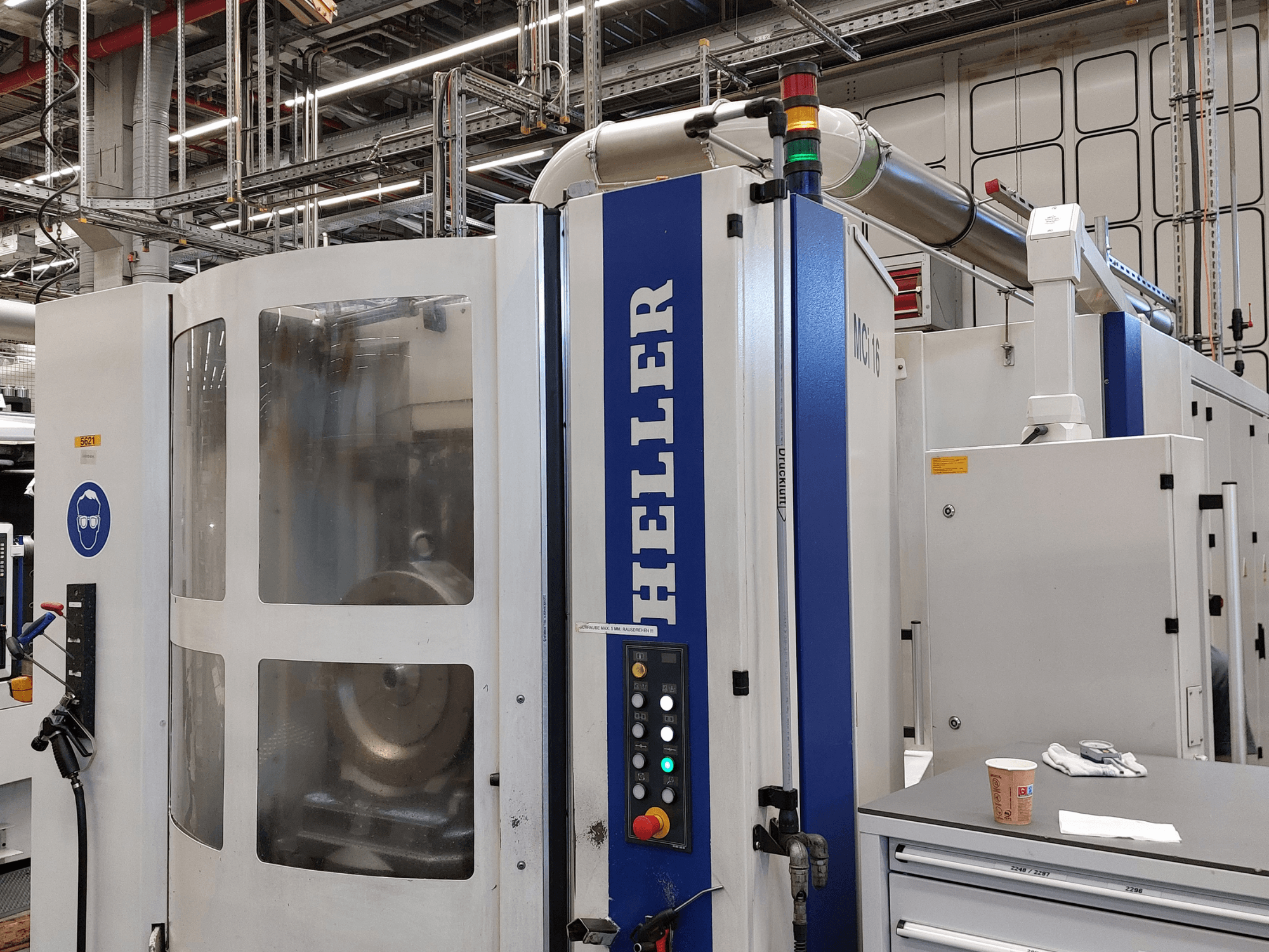 Heller MCI 16 vertical machining center in a factory setting, featuring control panel and safety signage.