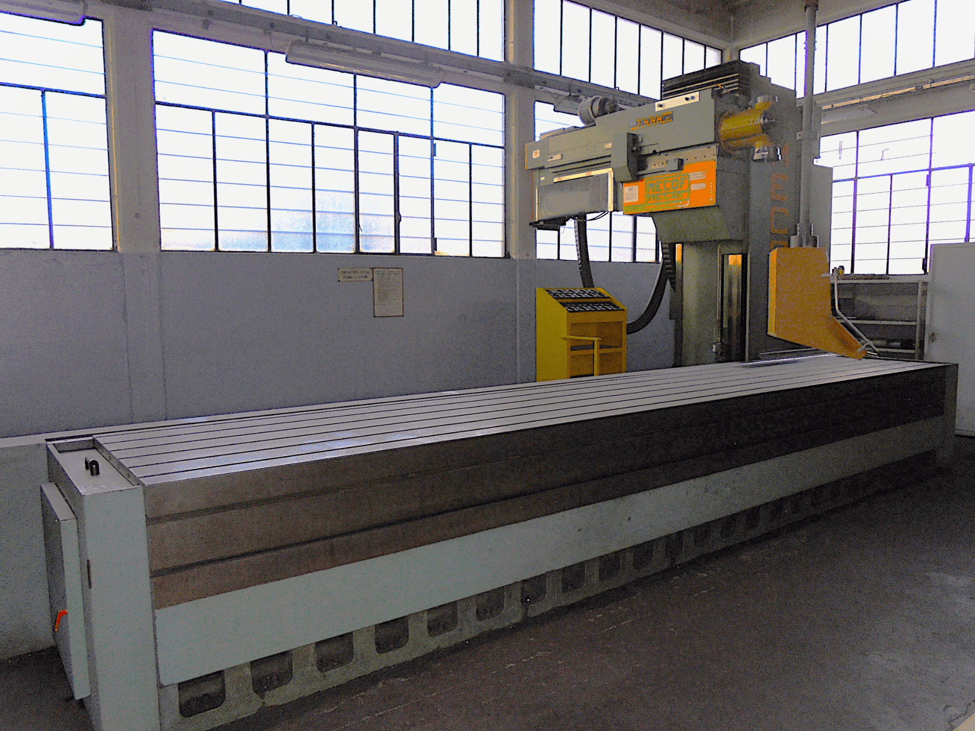 Brand unknown, vertical milling machine in a factory, side view, features a large table with grooved surface and control panel.