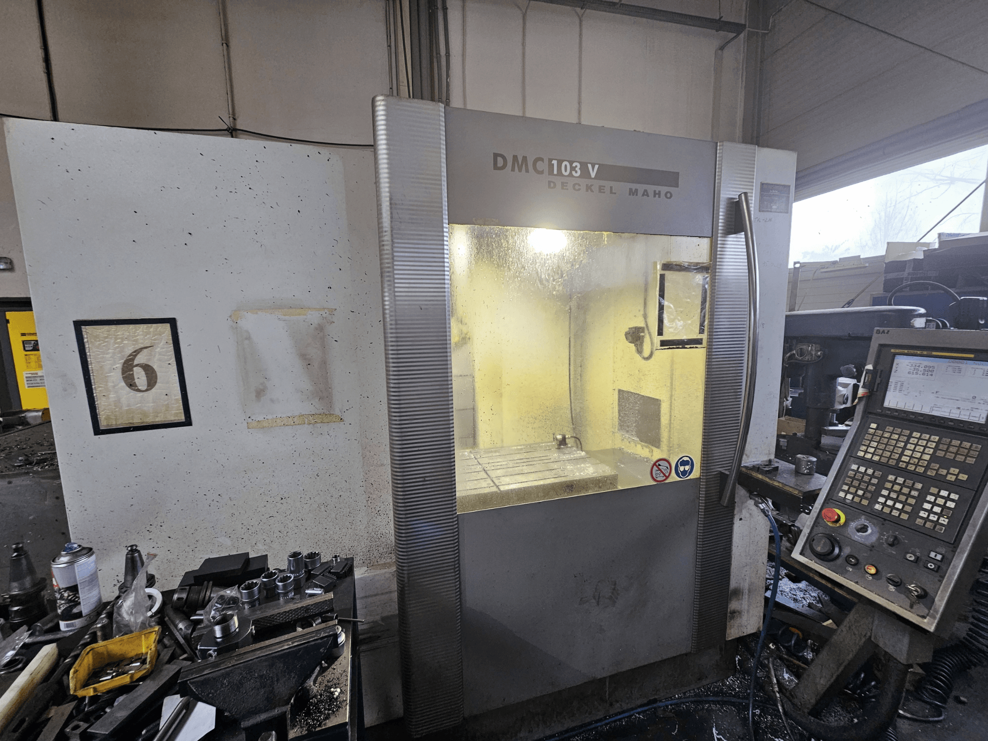 Front view of a Deckel Maho DMC 103 V CNC machine, showing control panel, work area, and numbered indicator "6."