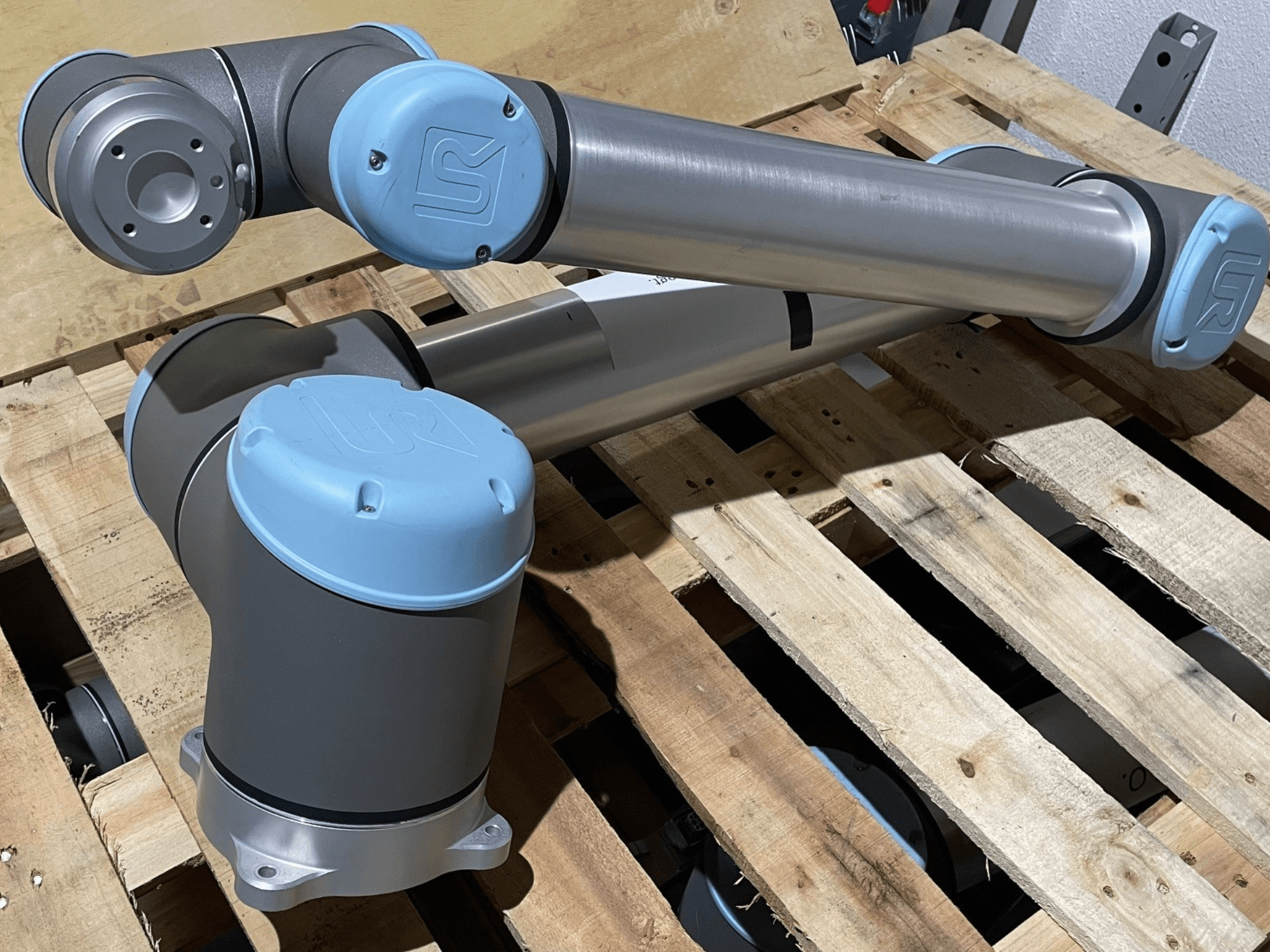 Silver robotic arm with blue end caps, front view, showcasing joints and mechanical details, resting on a wooden pallet.
