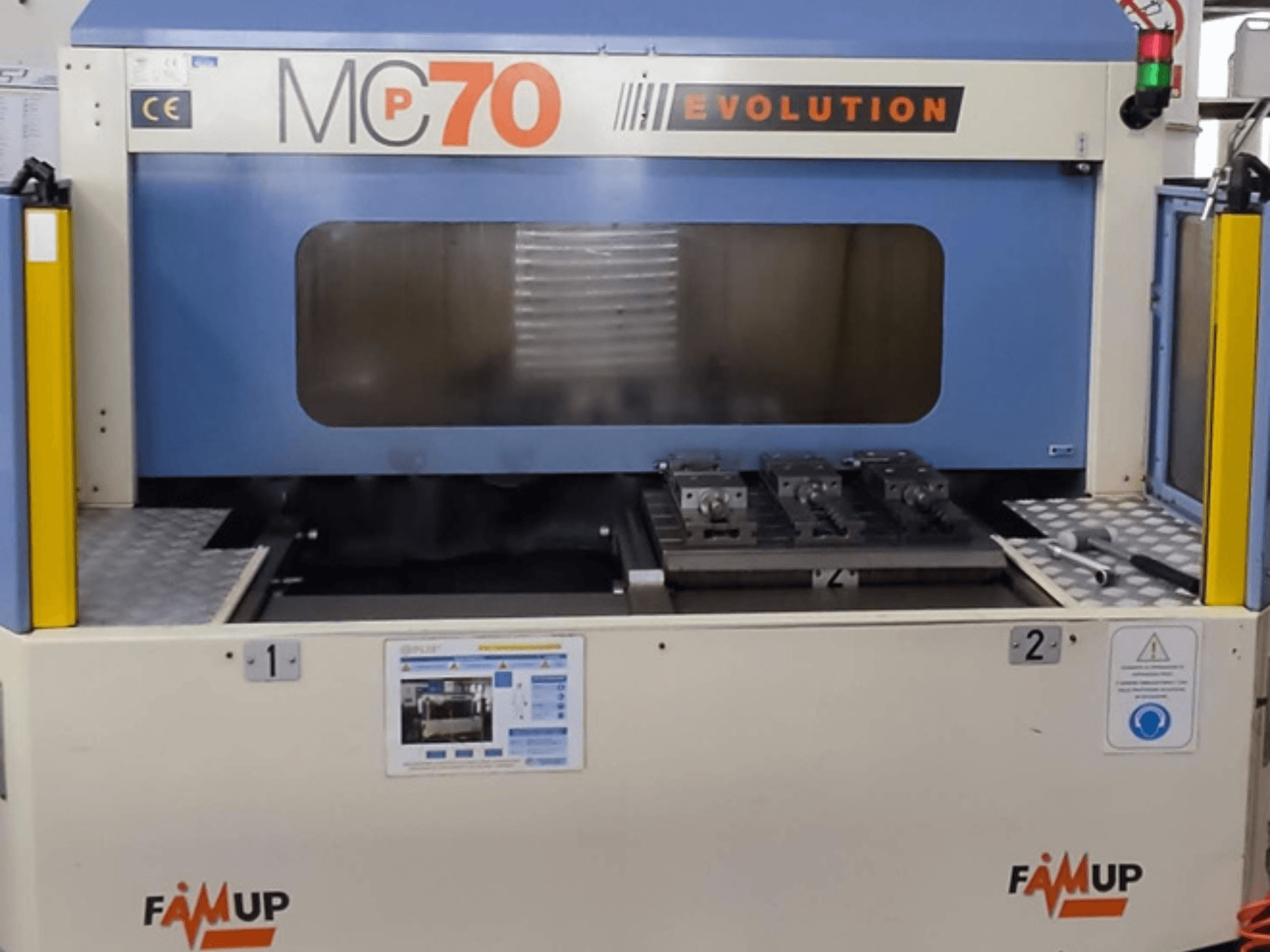 FAMUP MCP70 E vertical machining center, front view showing control panel and work area with fixtures and safety features.