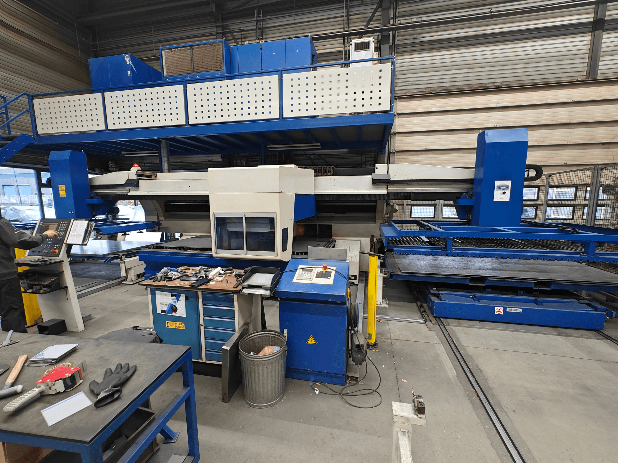 Industrial CNC machine from a front view, featuring blue and white construction, control panel, and various tools on the work table.