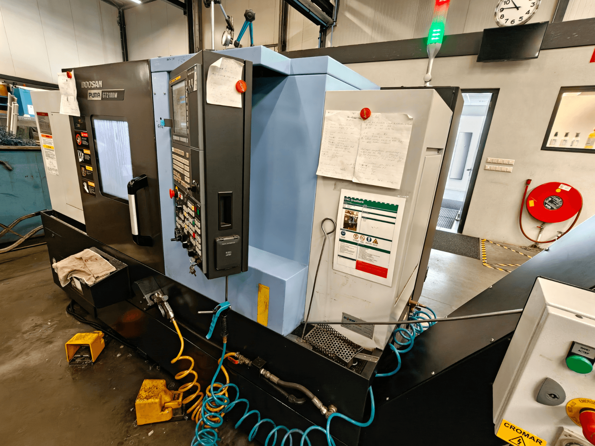 Front view of DOOSAN Puma GT 2100M horizontal turning machine with control panel, safety features, and maintenance notes visible.