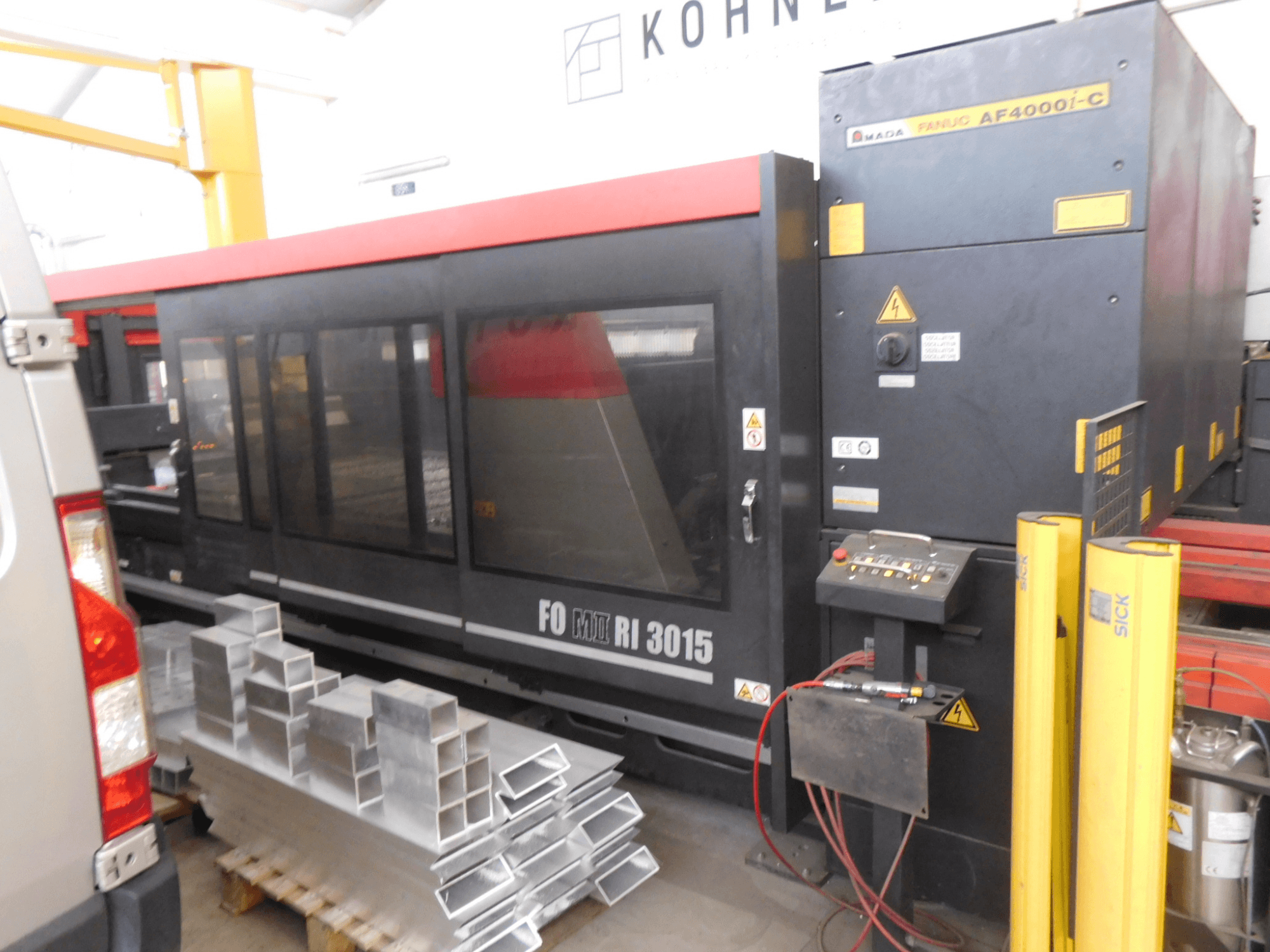 AMADA FO-3015 II RI CO2 laser cutting machine in a workshop, side view, showcasing control panel and stacked aluminum profiles.