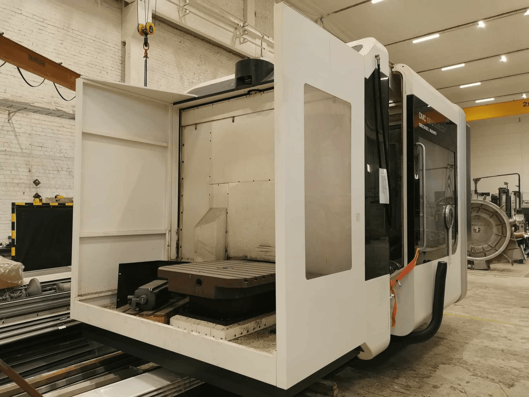 DMC 100U linear CNC machine, side view with open access door, showing work table and internal components.