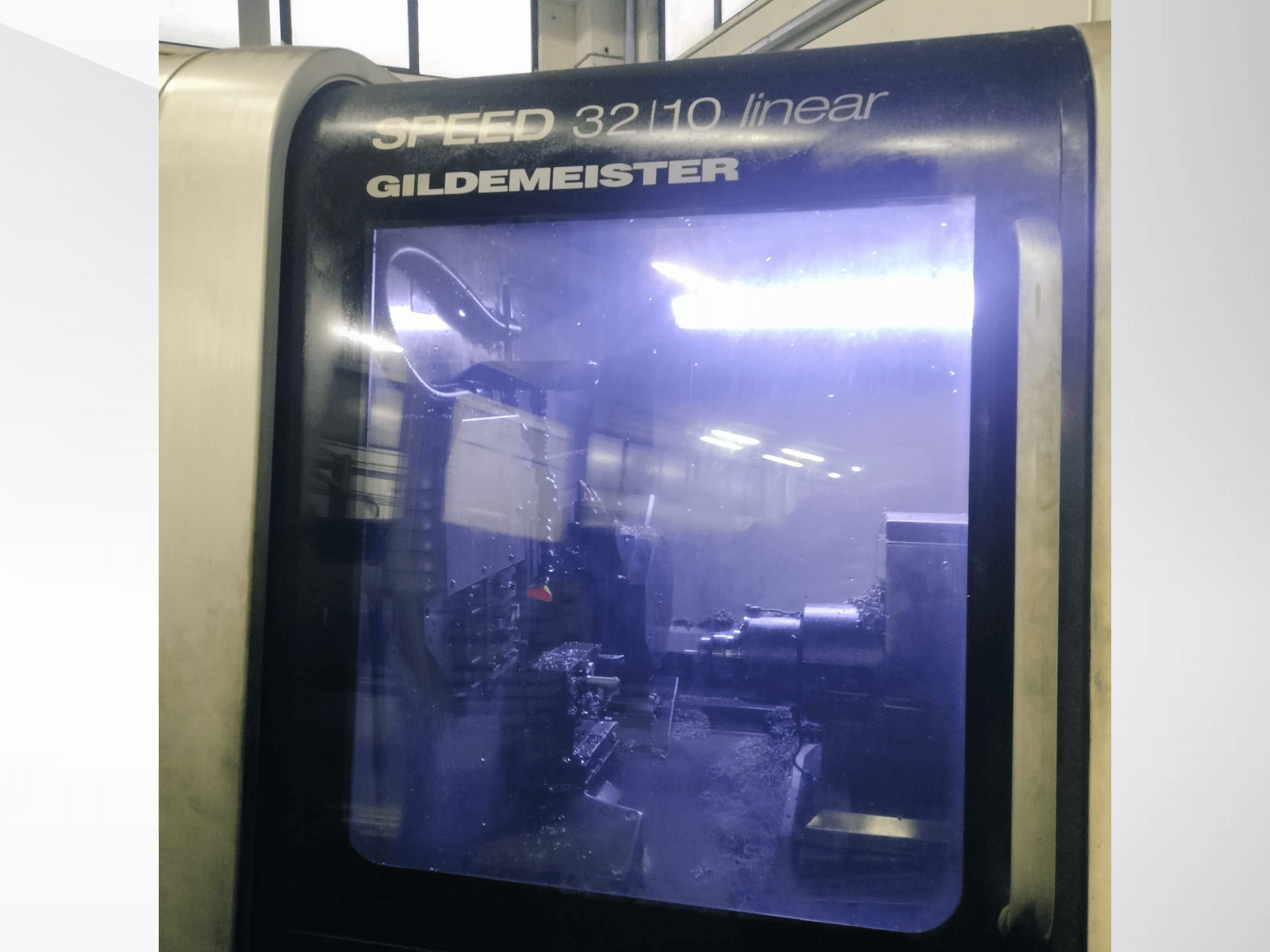 Gildemeister SPEED 3210 linear CNC machine front view, showing internal components and liquid coolant in operation.
