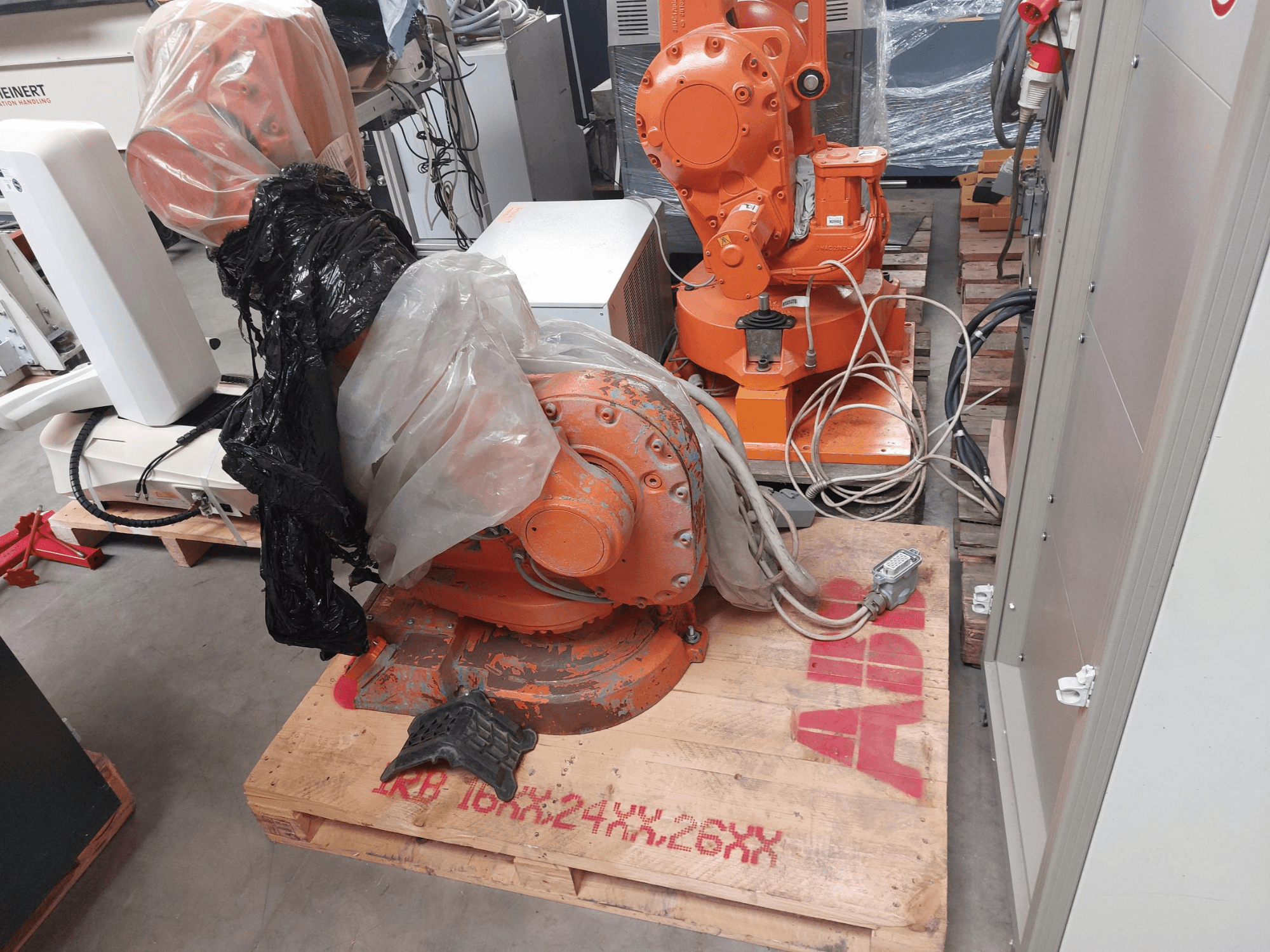 ABB IRB 1600 M2004 robot arm partially covered in plastic, viewed from the front, with cables and additional machinery nearby.