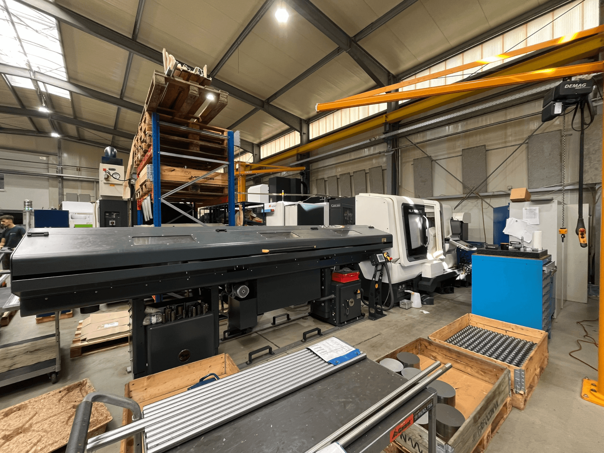 DMG MORI MORI NLX 2500/700 SY horizontal turning machine in a workshop, viewed from the side with storage and tools in background.