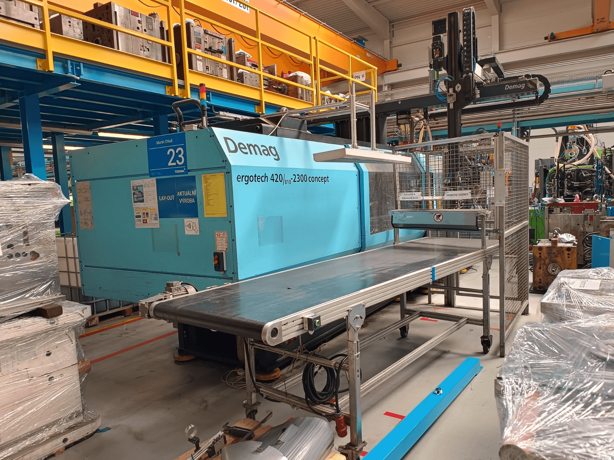 Demag ergotech 420/810 - 2300 hydraulic injection moulding machine in side view, featuring a conveyor and safety enclosure.
