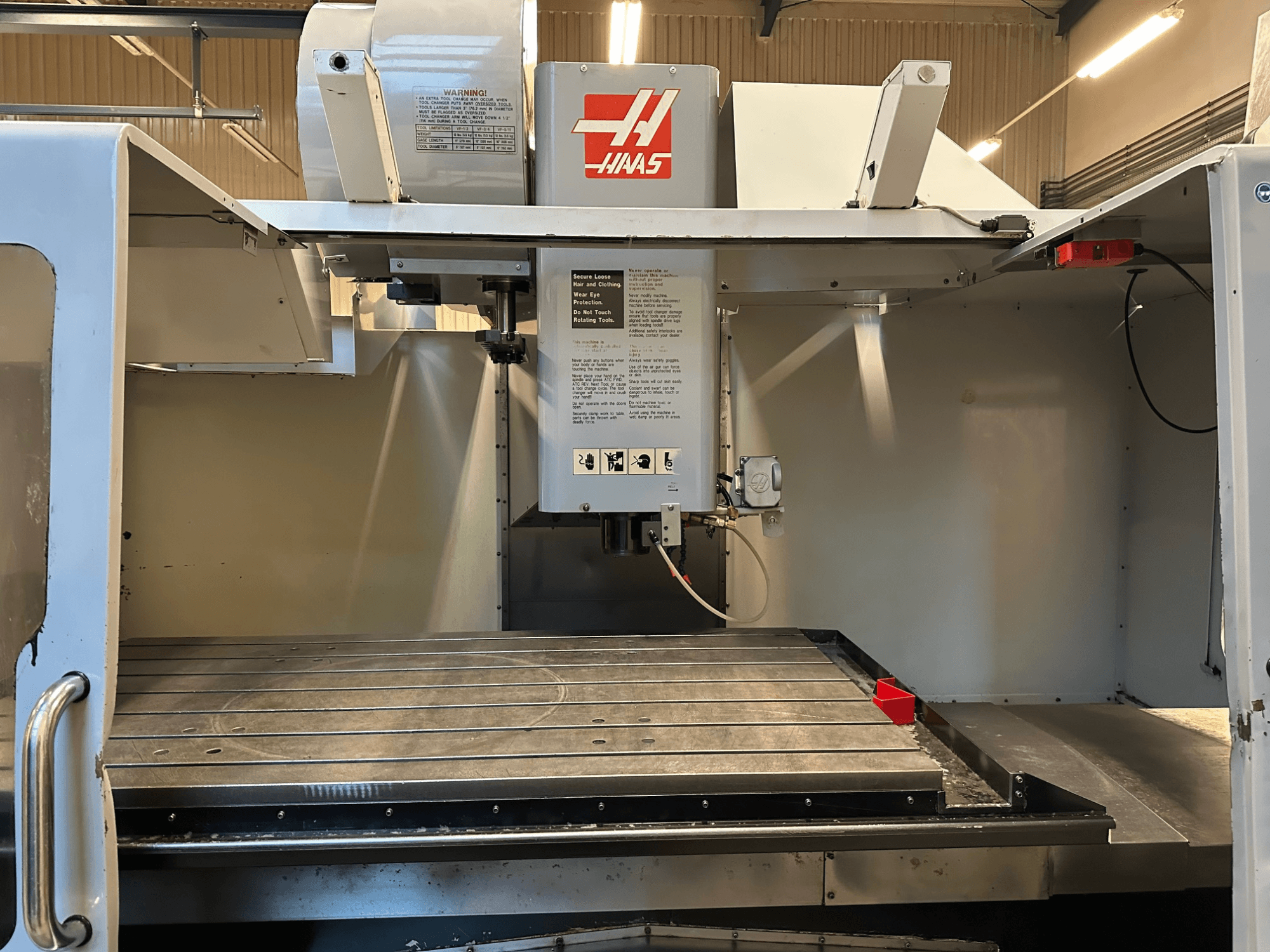 Haas CNC milling machine, model VF-2, front view showing controls, metal work table, and safety label on the panel.