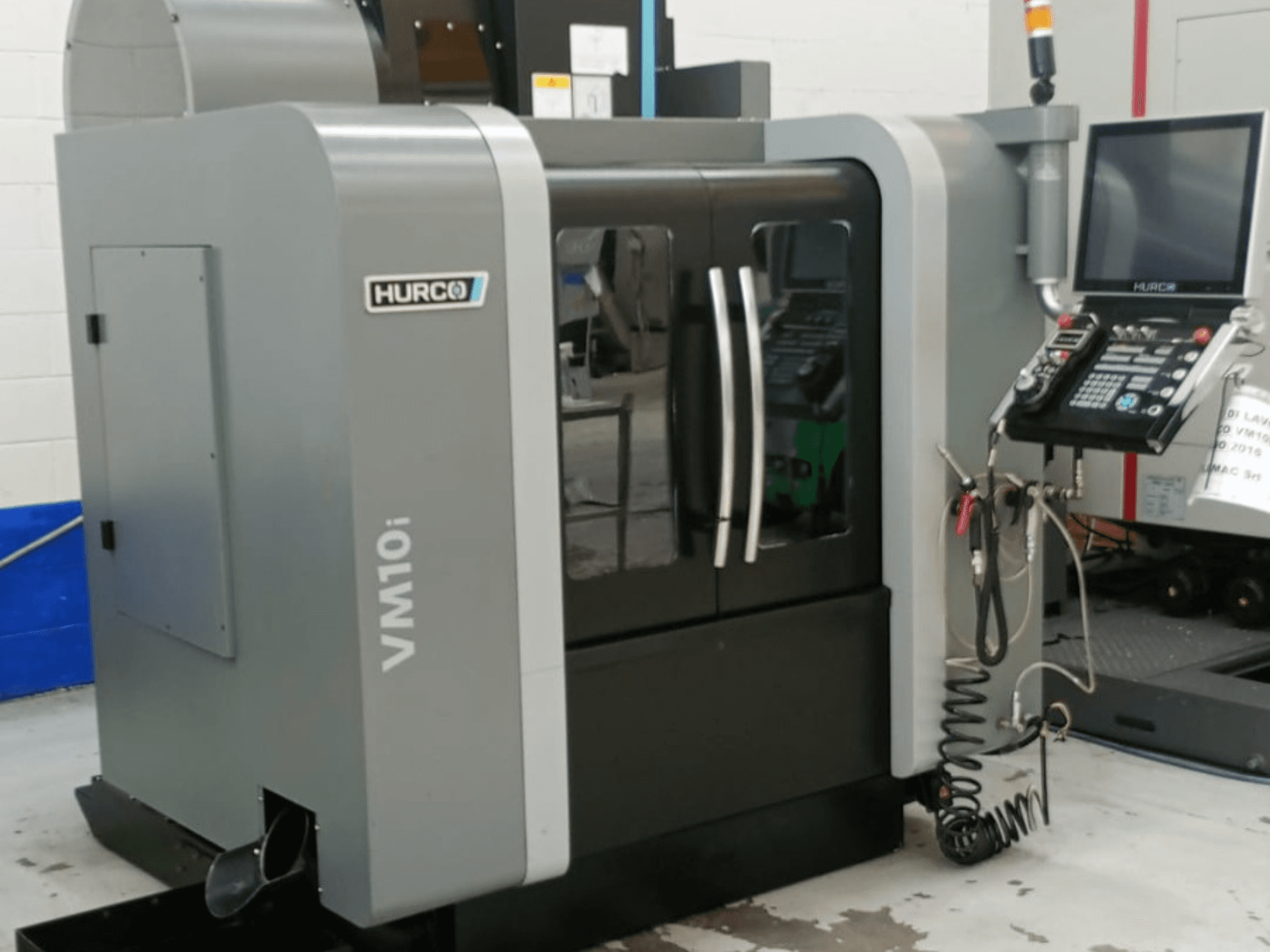 Hurco VM10i vertical machining center in side view, featuring dual doors, control panel, and visible cables for operation.