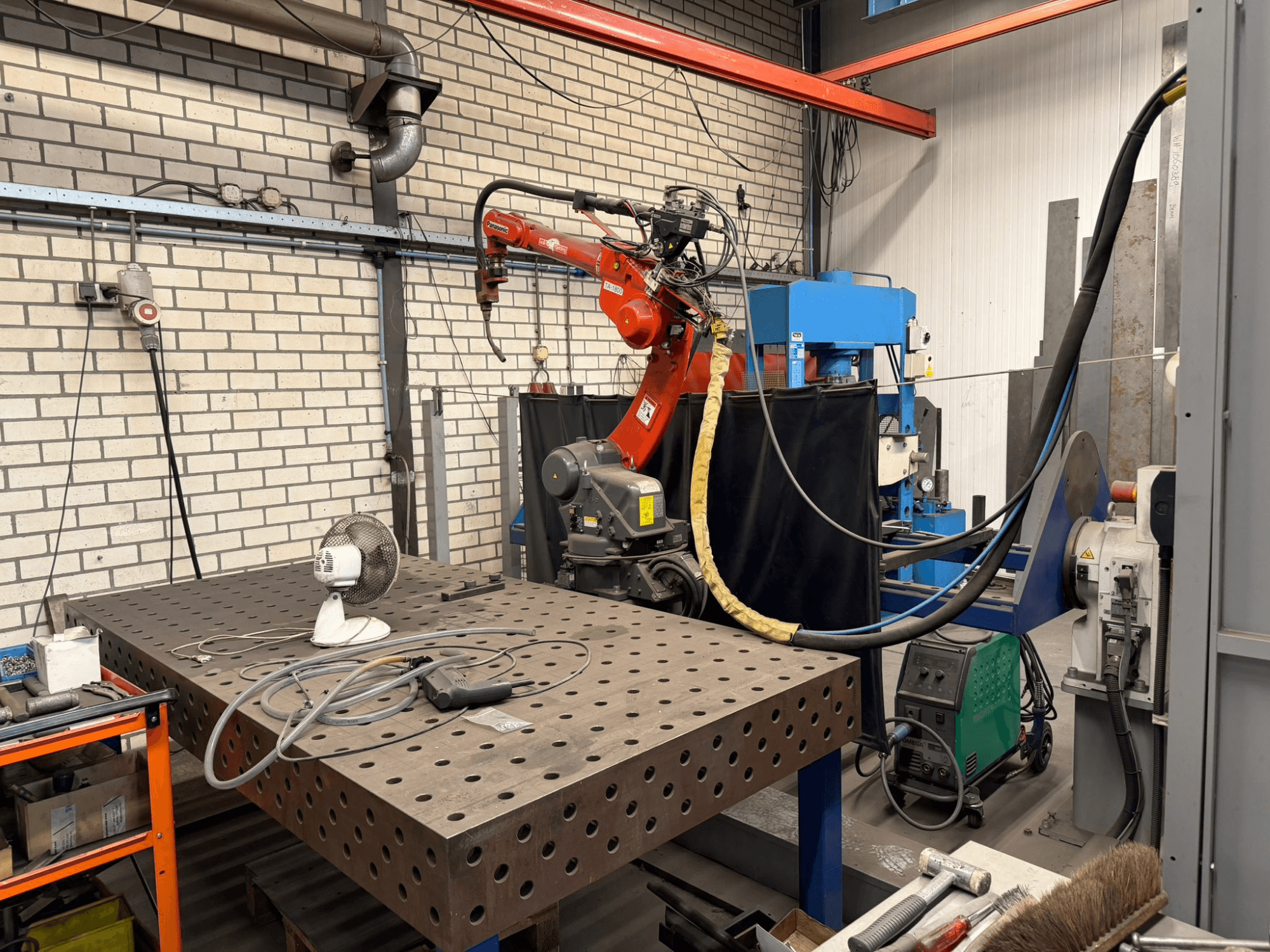 Front view of a PANASONIC TA-1800 welding robot on a workstation, with a fan and welding equipment visible.
