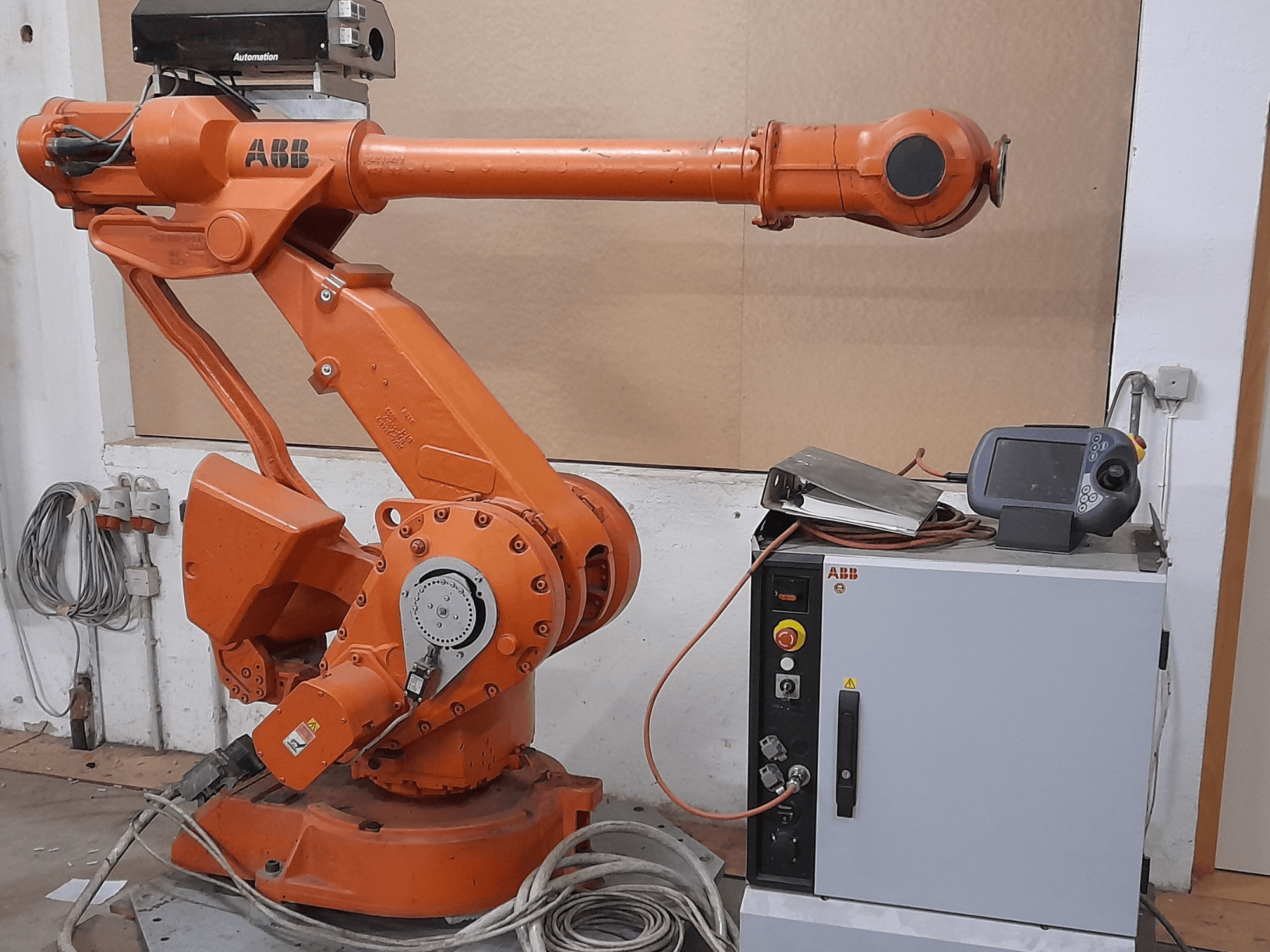 Orange ABB robotic arm with a control panel, front view, showcasing cables and automation equipment.