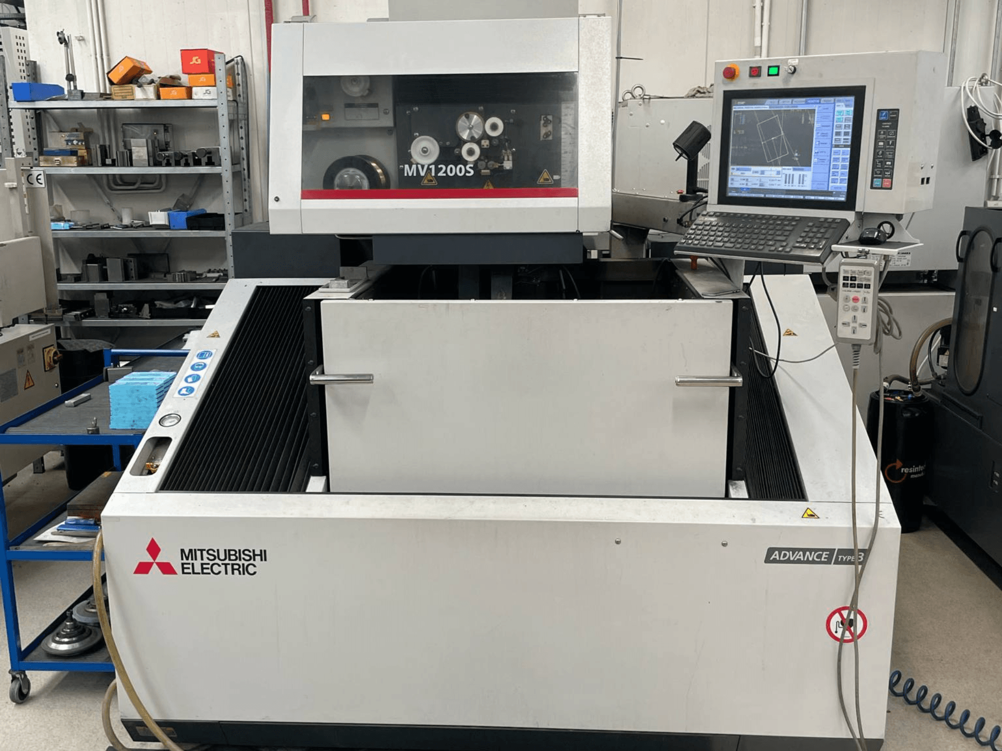 Mitsubishi MV1200S Wire EDM machine in front view, featuring control panel and work area, with safety warnings visible.