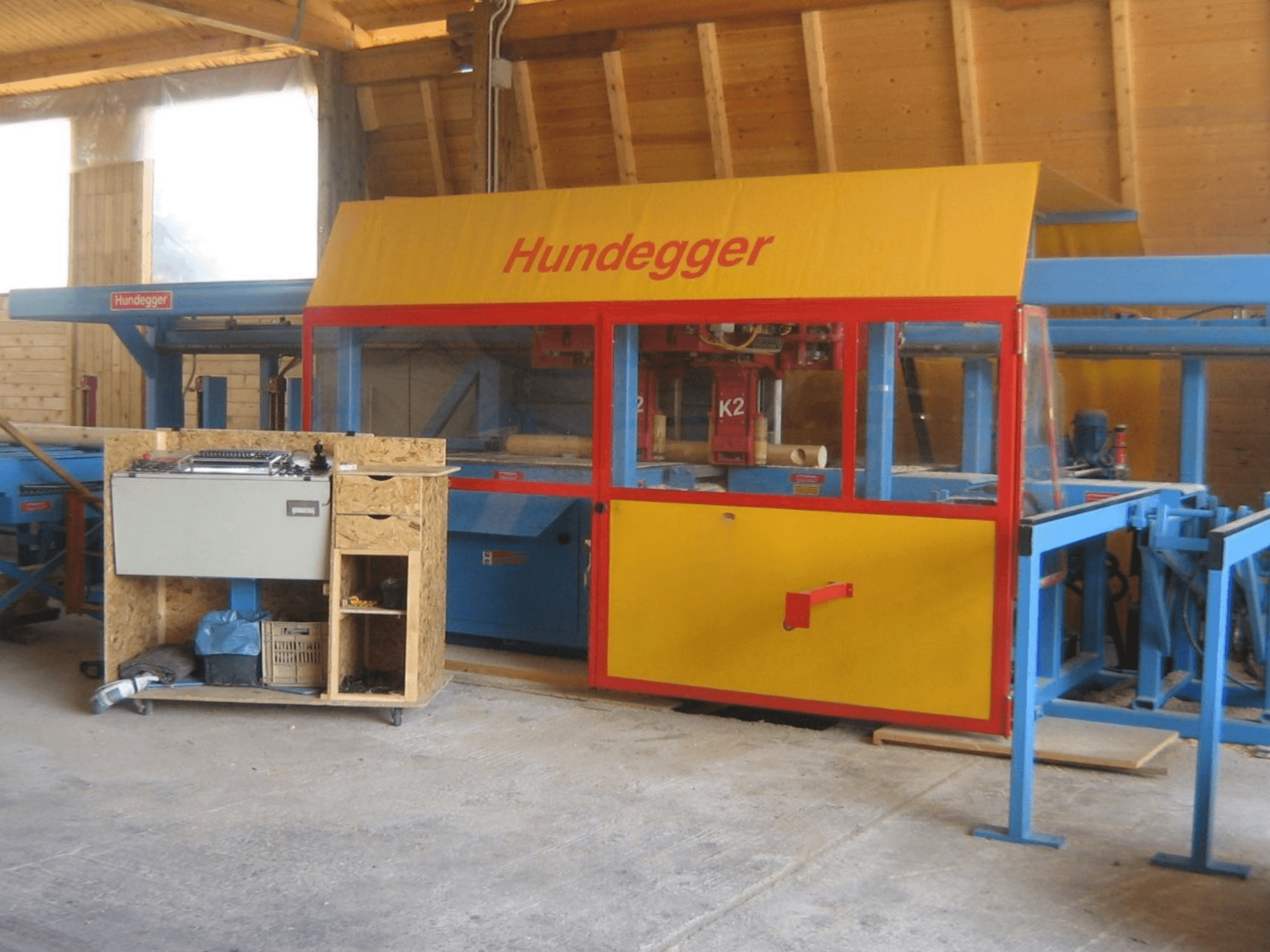 CNC Wood Machining Centre HUNDEGGER K2 4 assi in a workshop, front view showing yellow and blue design with worktable.