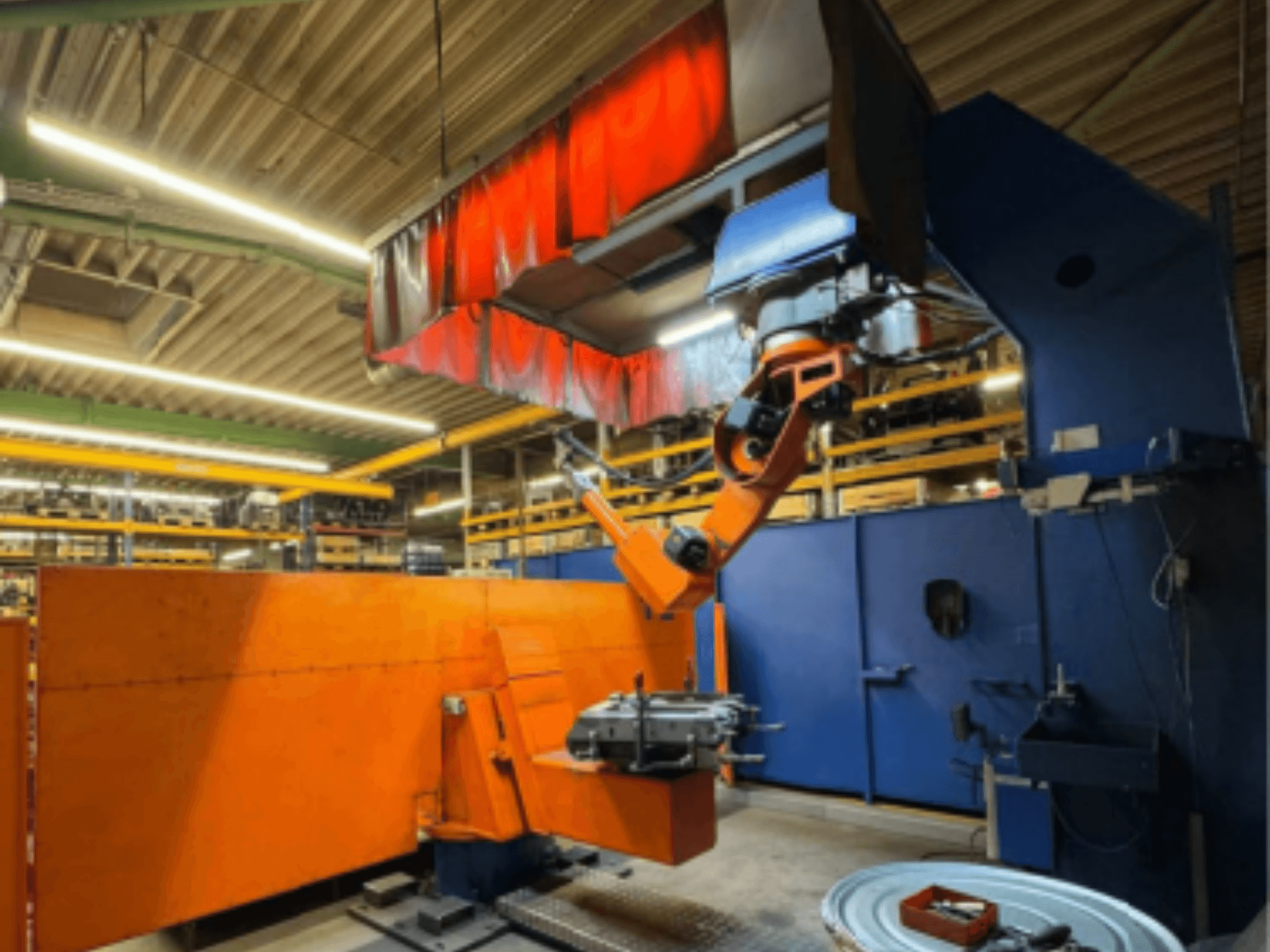CLOOS Romat 350 e welding robot in an industrial setting, front view with orange arm, holding a workpiece under overhead curtain.