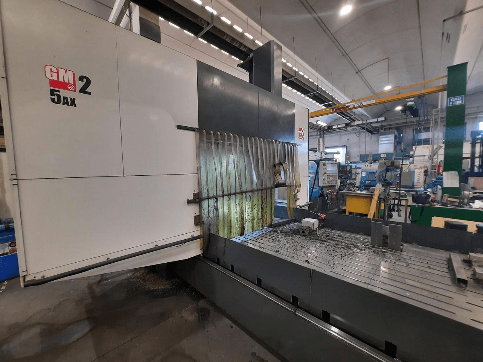 GM 2 5AX CNC machine in a workshop, side view, showing operational area and metal shavings on the bed surface.