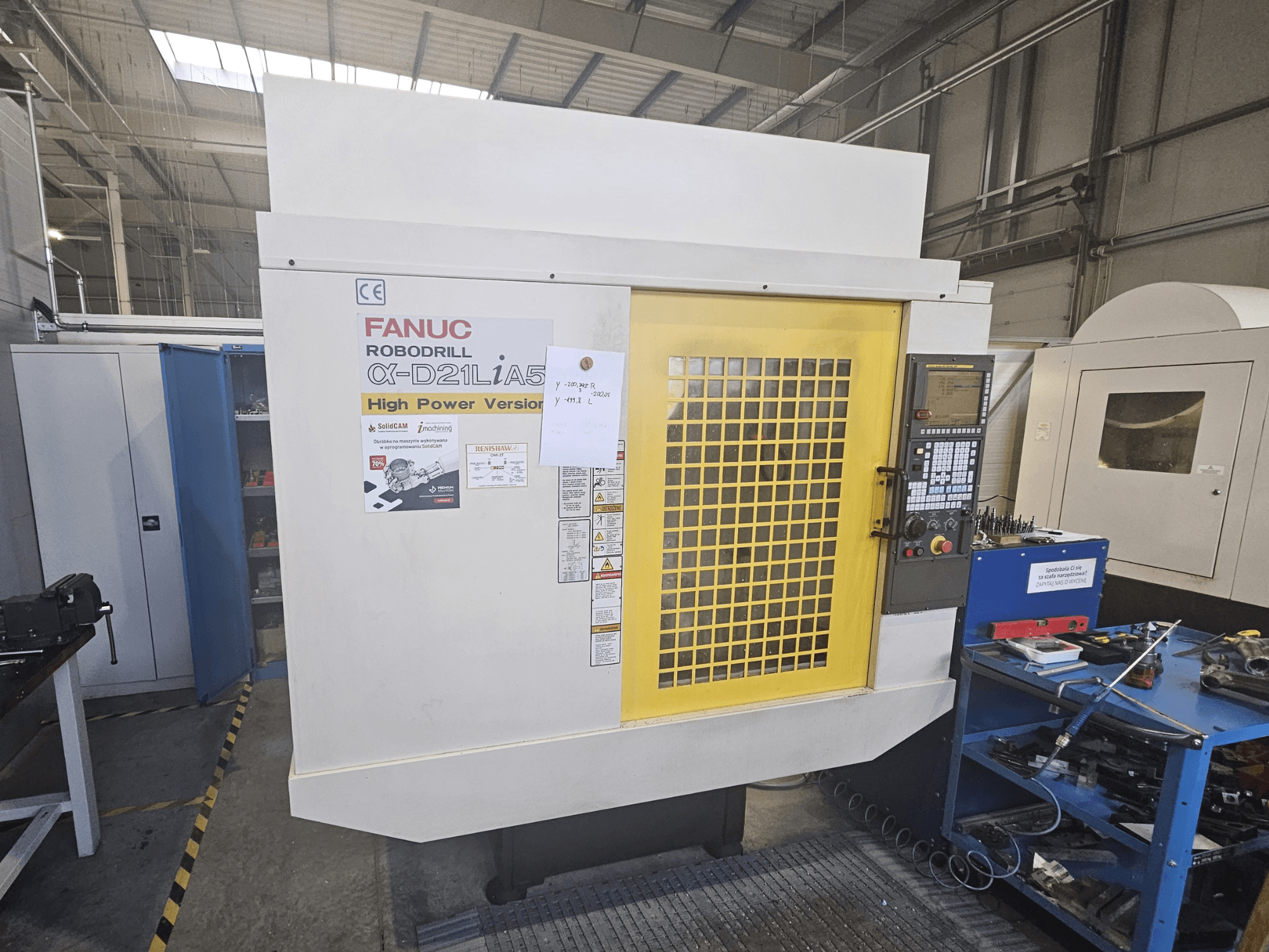 Front view of a FANUC Robodrill α-D21LiA5 with yellow safety door, control panel, and workspace tools nearby.
