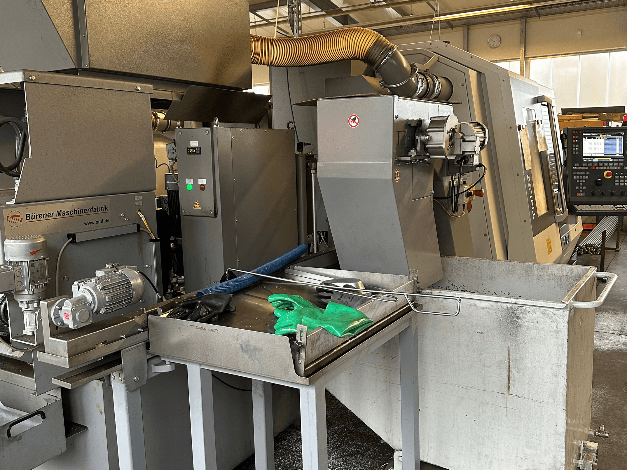 TRAUB TNL32-9 Swiss Type Turning Machine, side view, showcasing control panel, motor, and cutting area with metal shavings.
