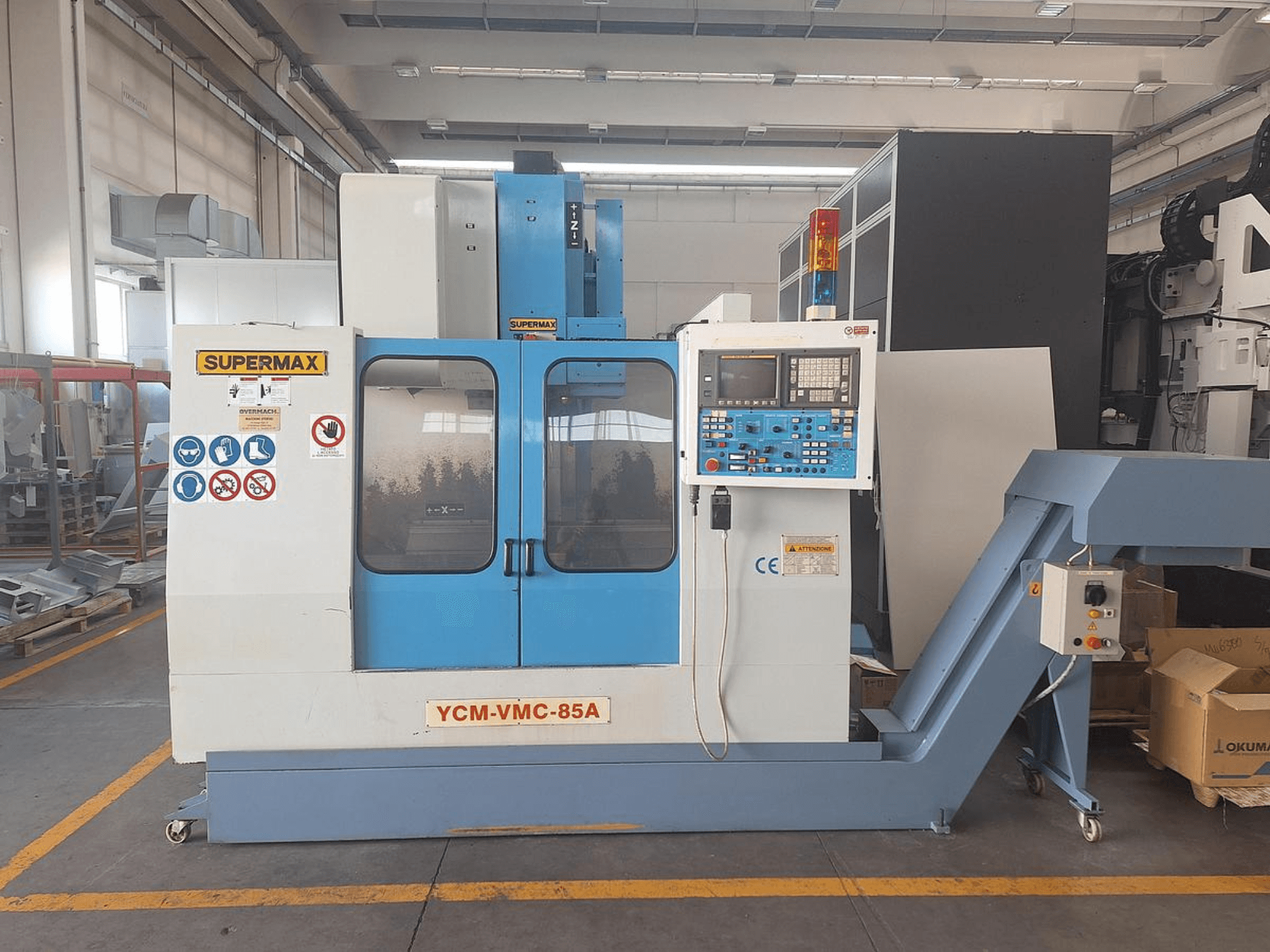 Vertical Machining Centre SUPERMAX YCM-VMC-85A in a factory with control panel and safety decals, front view.