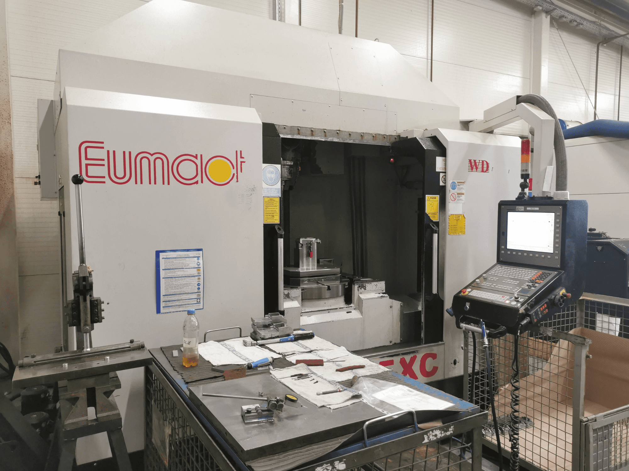 Front view of a Eumdaot CNC machine with control panel, tools, and a work surface cluttered with components and materials.