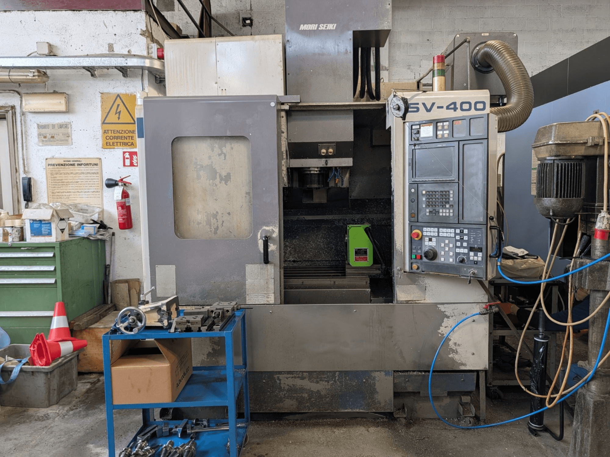 MORI SEIKI SV-400 vertical machining centre in a workshop, side view, showcasing control panel and machine tools nearby.