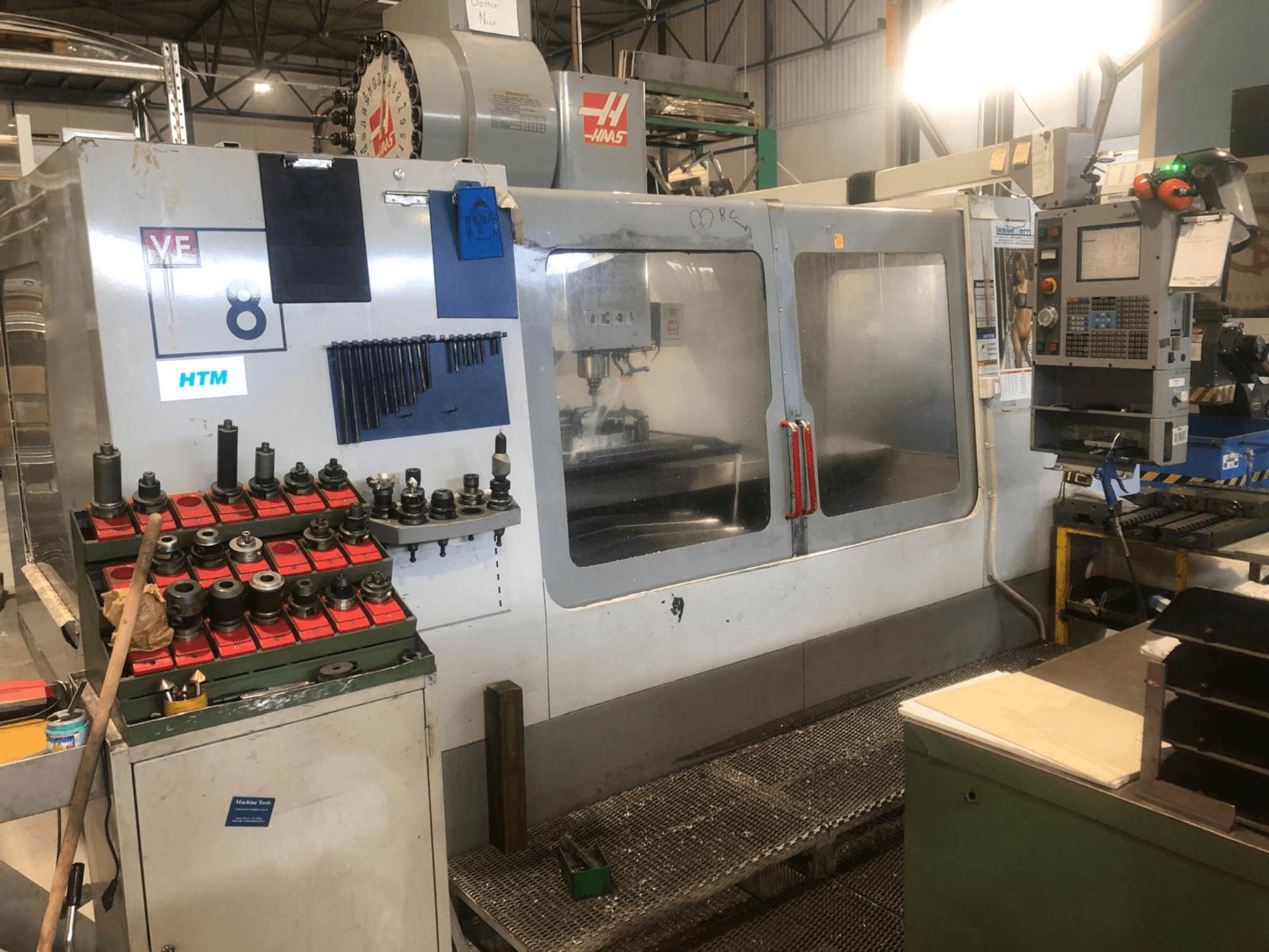 Haas CNC machine in a workshop, front view; displays tools and controls, with visible model details and organized tool holders.