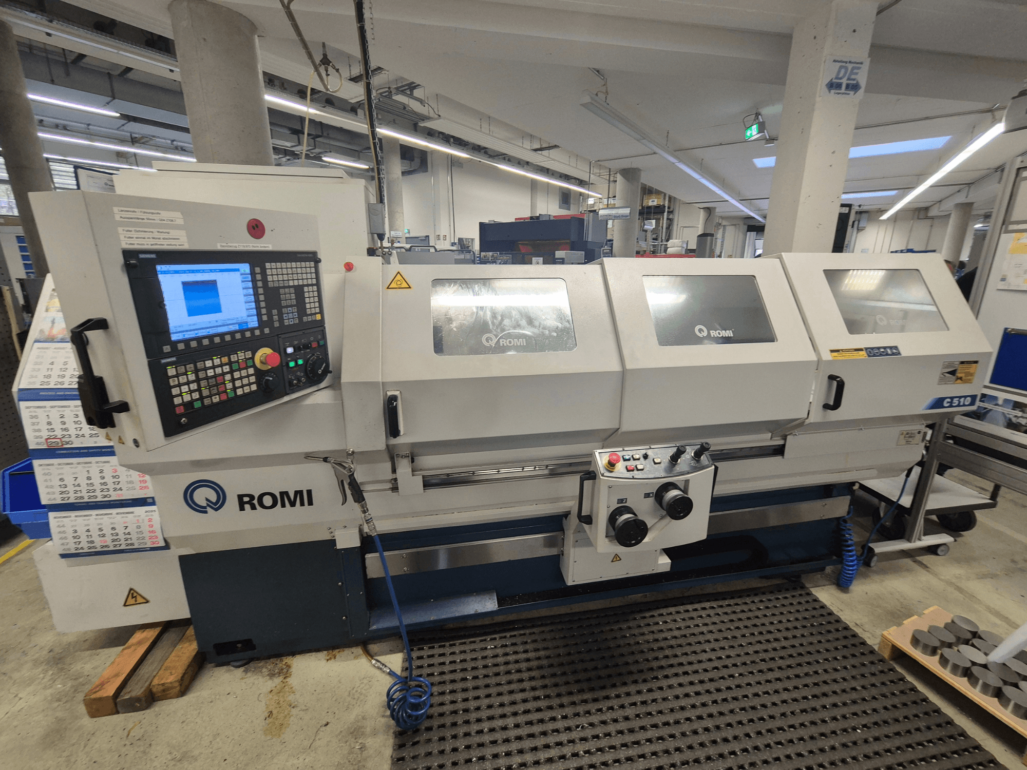Romi C510 lathe viewed from the front, featuring a digital control panel and three protective covers. Includes safety warning labels.
