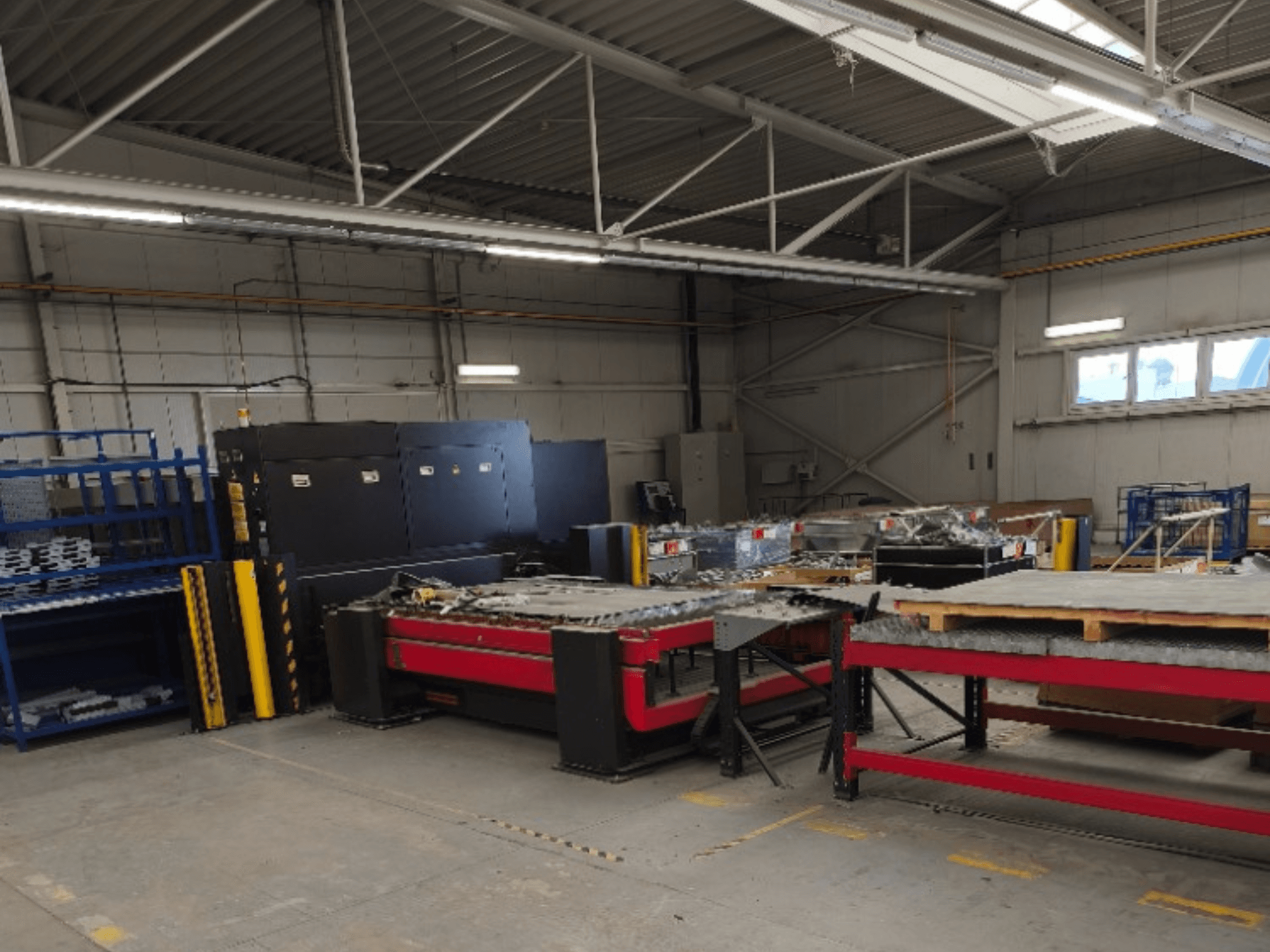 AMADA LCG 3015 AJ fiber laser cutting machine in a workshop, visible from the front with storage racks and materials in the background.