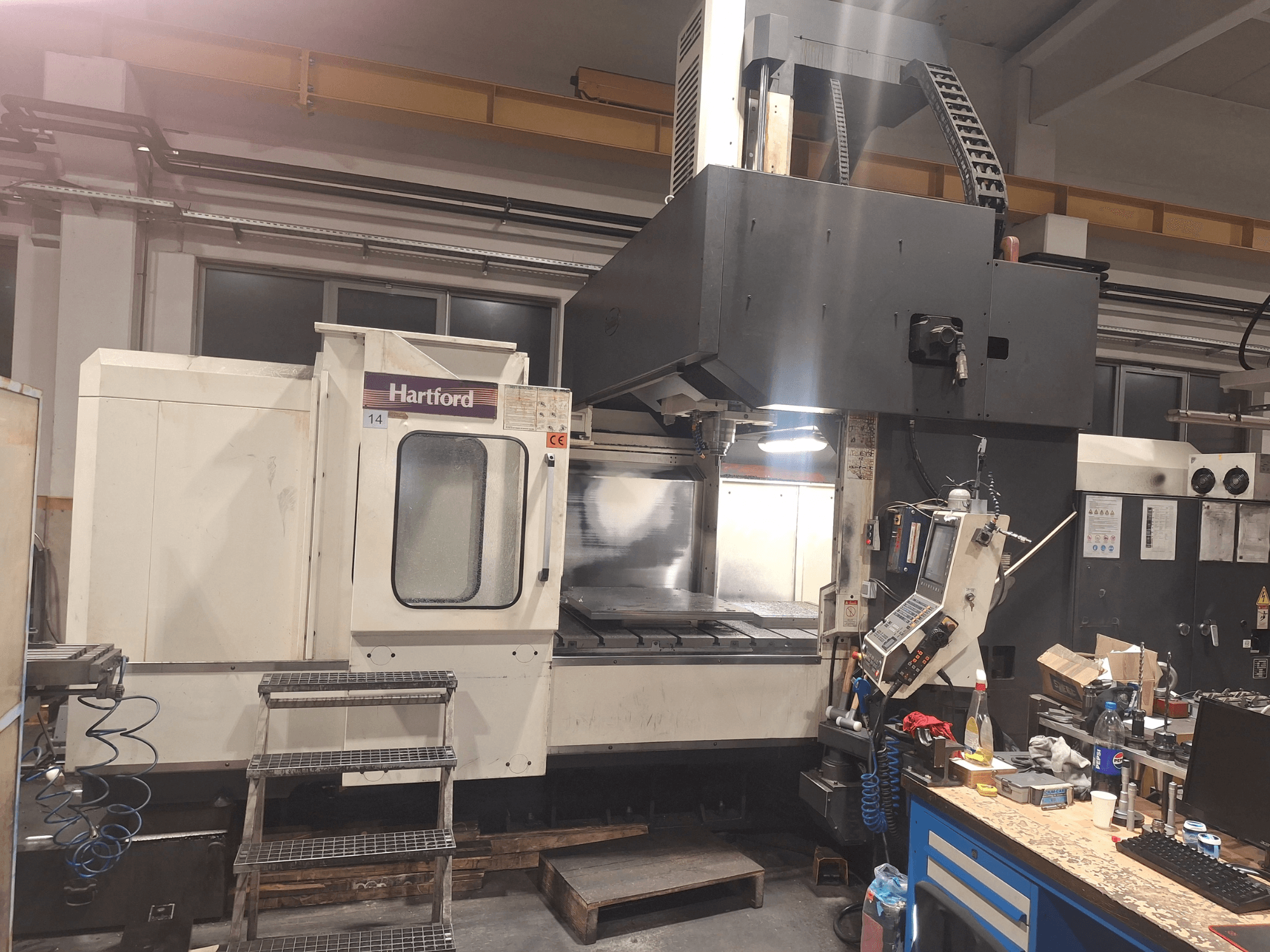 Hartford CNC machine, front view, with technical controls, steps to access, and a work table area, in a workshop setting.