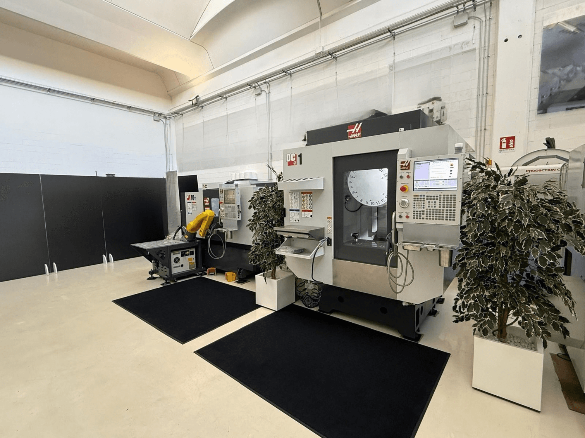 Front view of a HAAS DC-1 Vertical Machining Centre in a clean workspace, featuring a touchscreen control panel and surrounding plants.