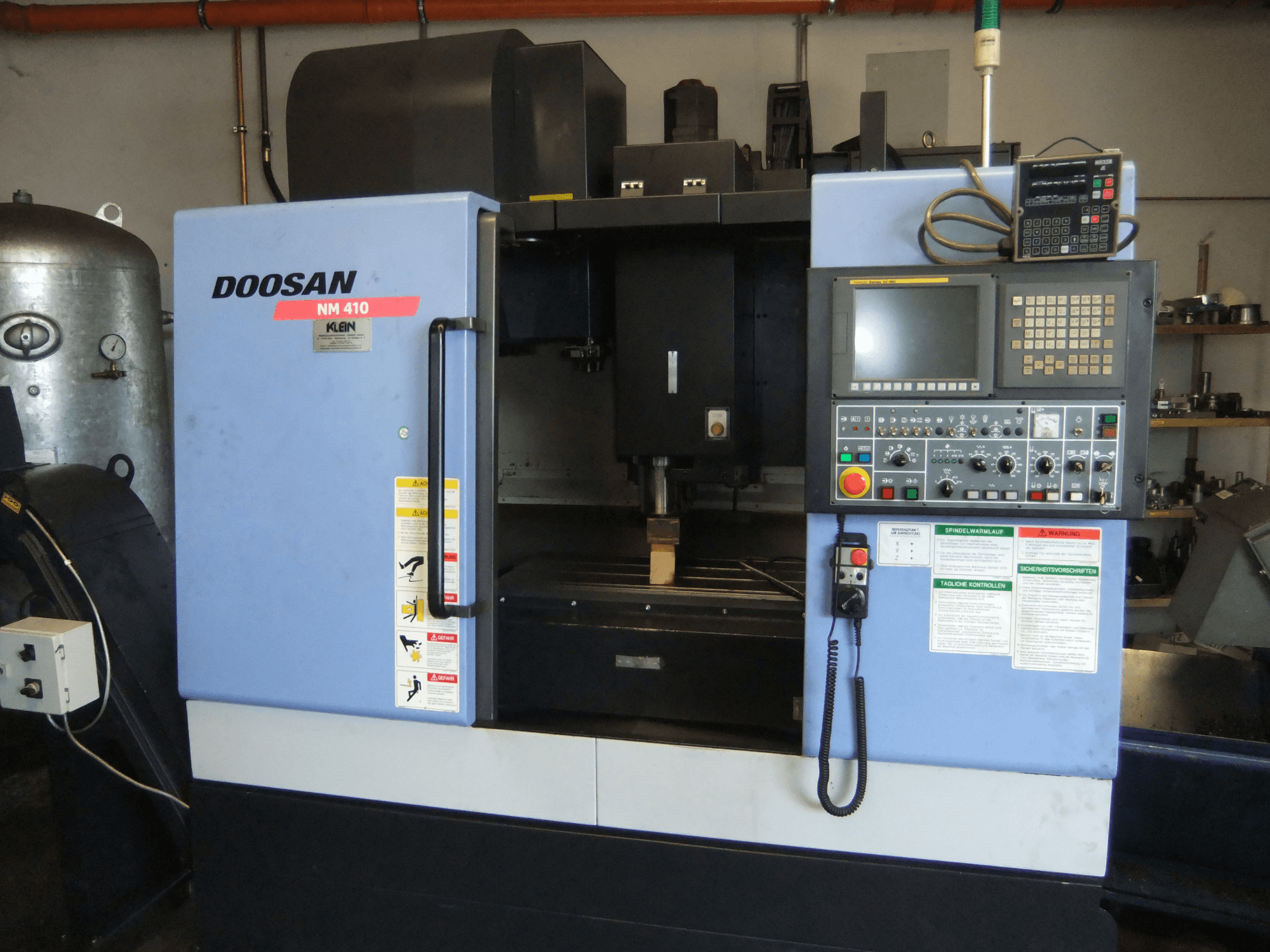DOOSAN NM 410 vertical machining centre, front view, showcasing control panel, spindle area, and safety labels.