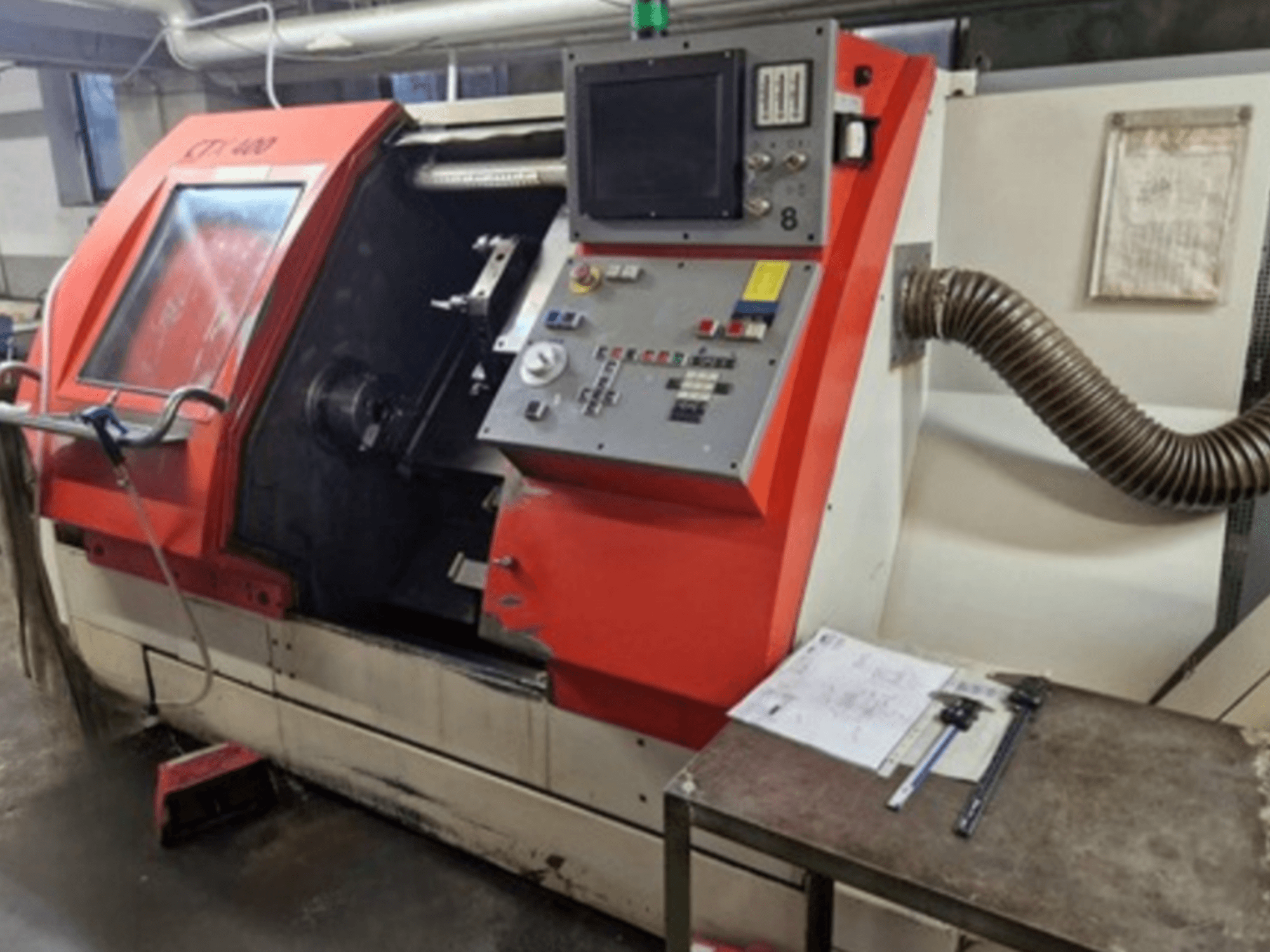 Gildemeister CTX 400 horizontal turning machine in front view, showcasing control panel, open door, and workshop table with tools.