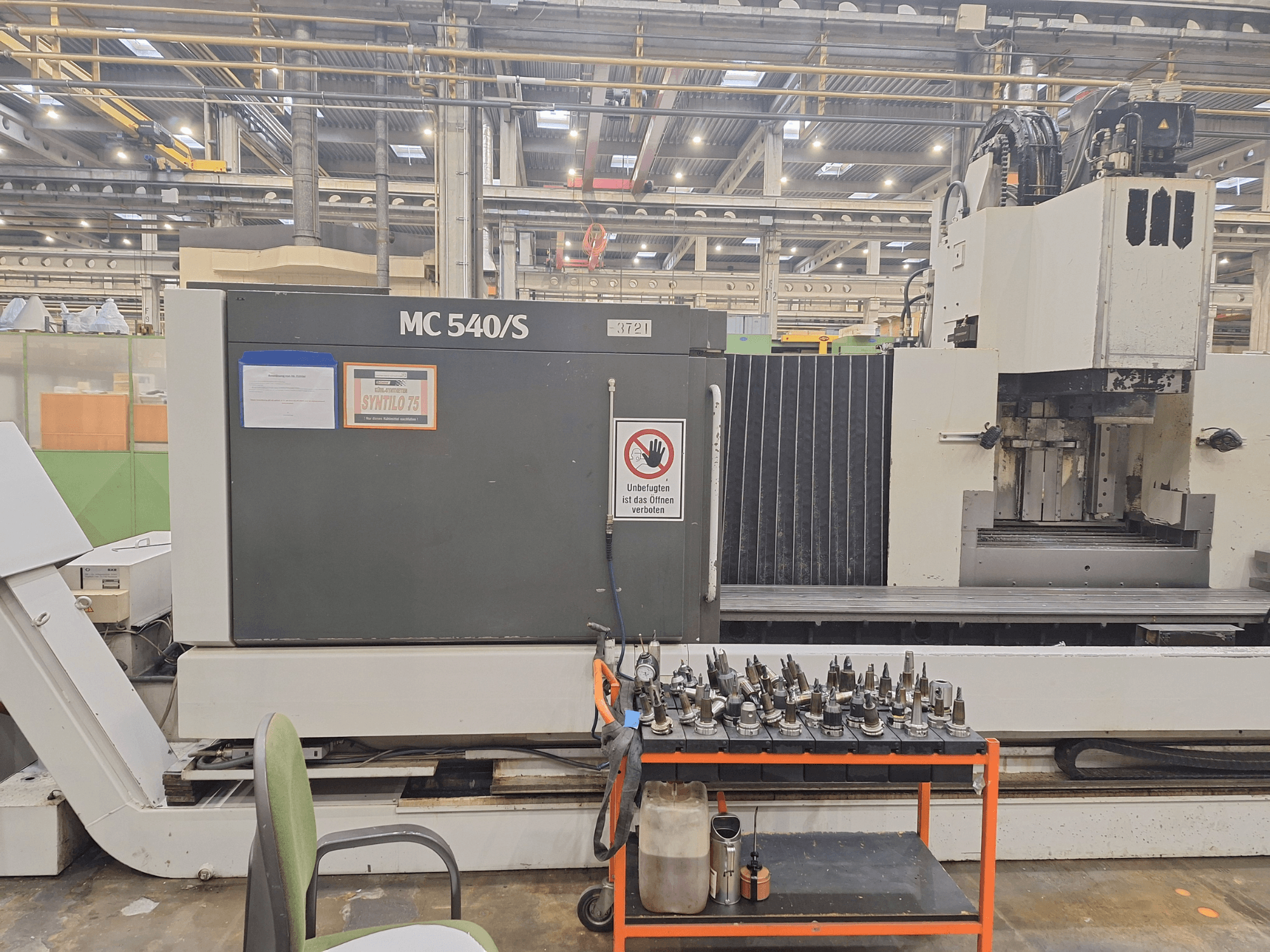 Vertical machining center STAMA MC 540S in a workshop, side view with tool holders on a cart nearby.