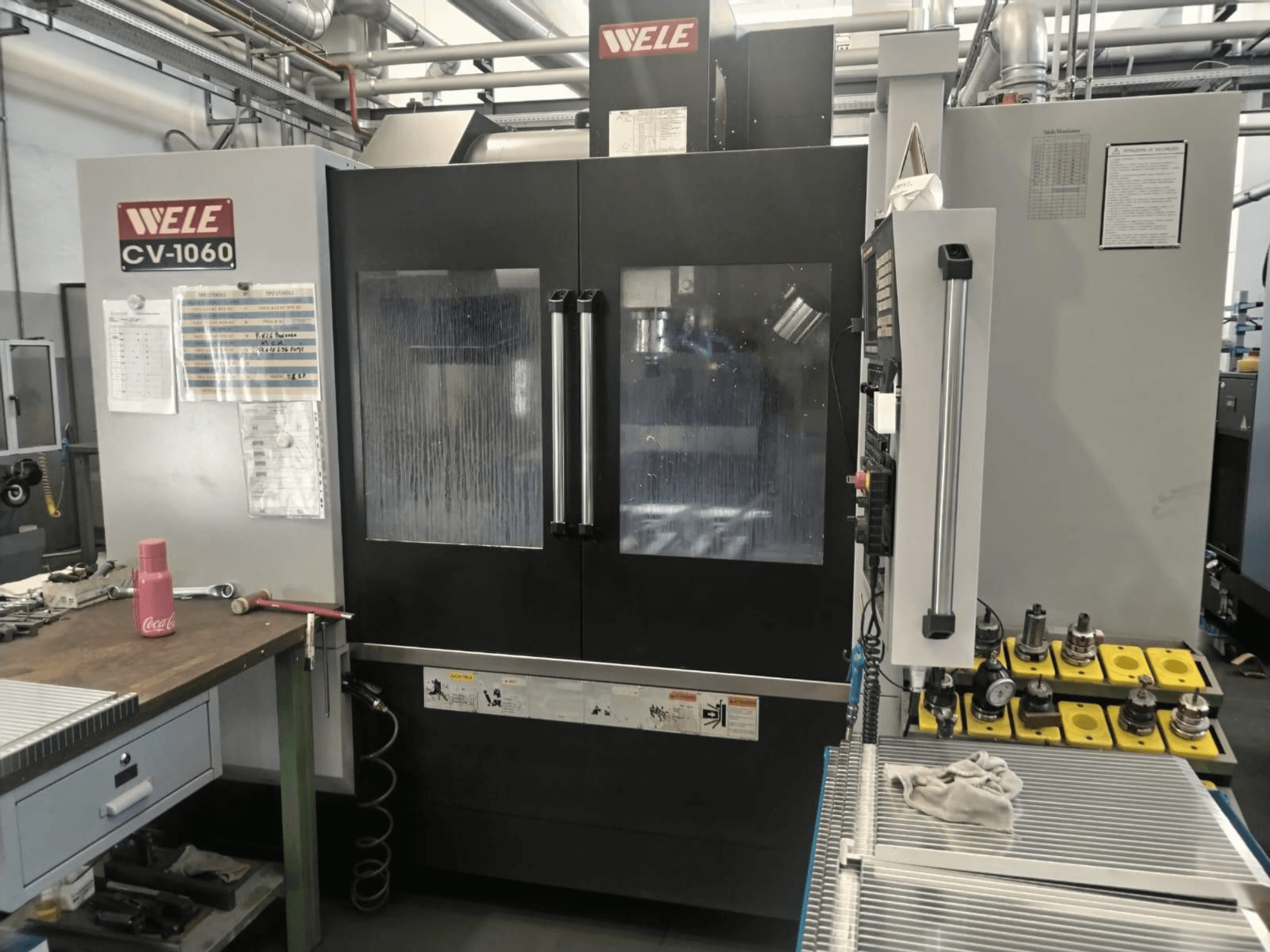 Wele CV-1060 vertical machining centre, front view, with control panel and visible workspace; includes accessory tools and safety labels.