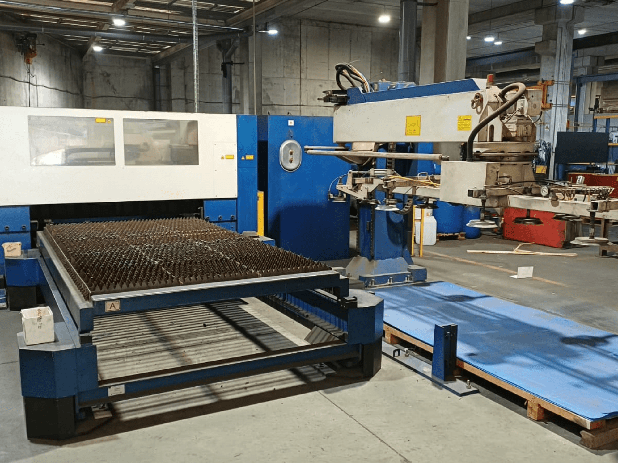 TRUMPF TRUMATIC L 3030 CO2 laser cutting machine, side view, showcasing the cutting table with spiked surface and robotic arm.