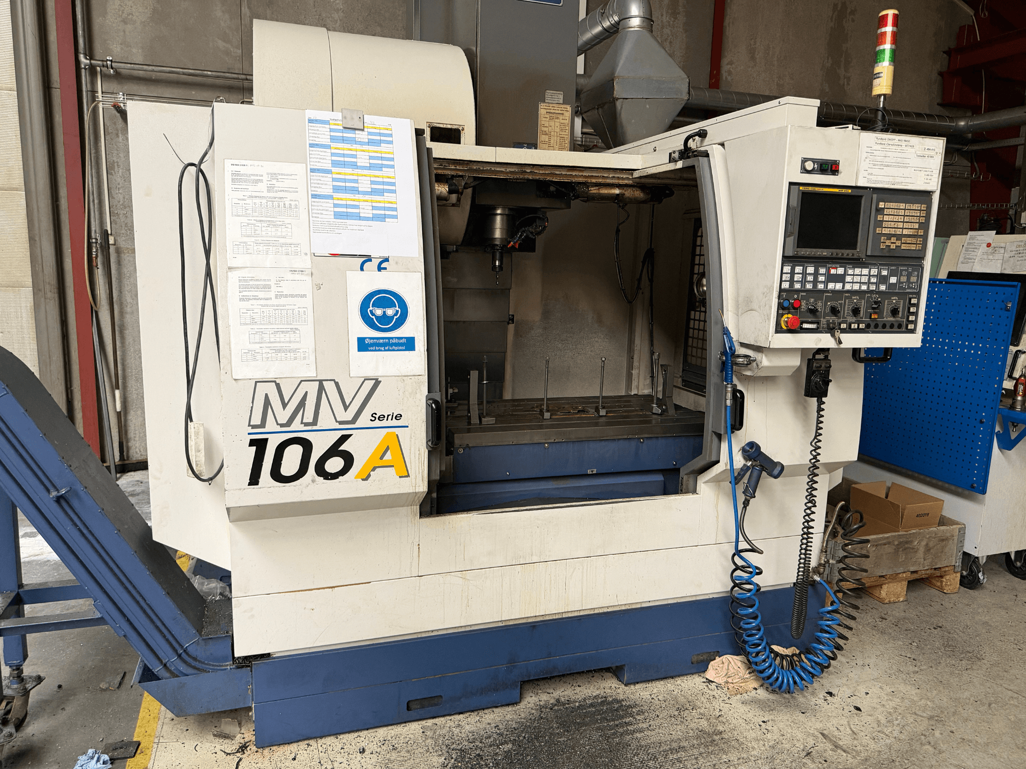 YCM MV106A Vertical Machining Centre, front view featuring control panel and workspace, with technical documentation attached.