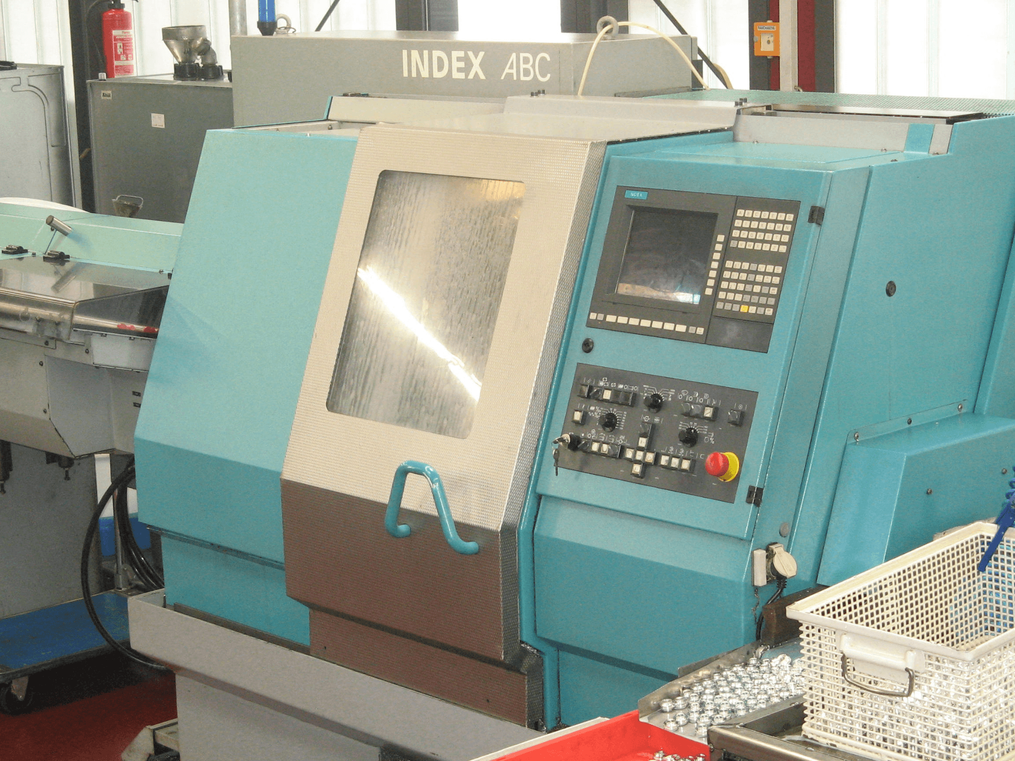 Front view of an INDEX ABC horizontal turning machine with control panel and visible workpieces on a nearby tray.