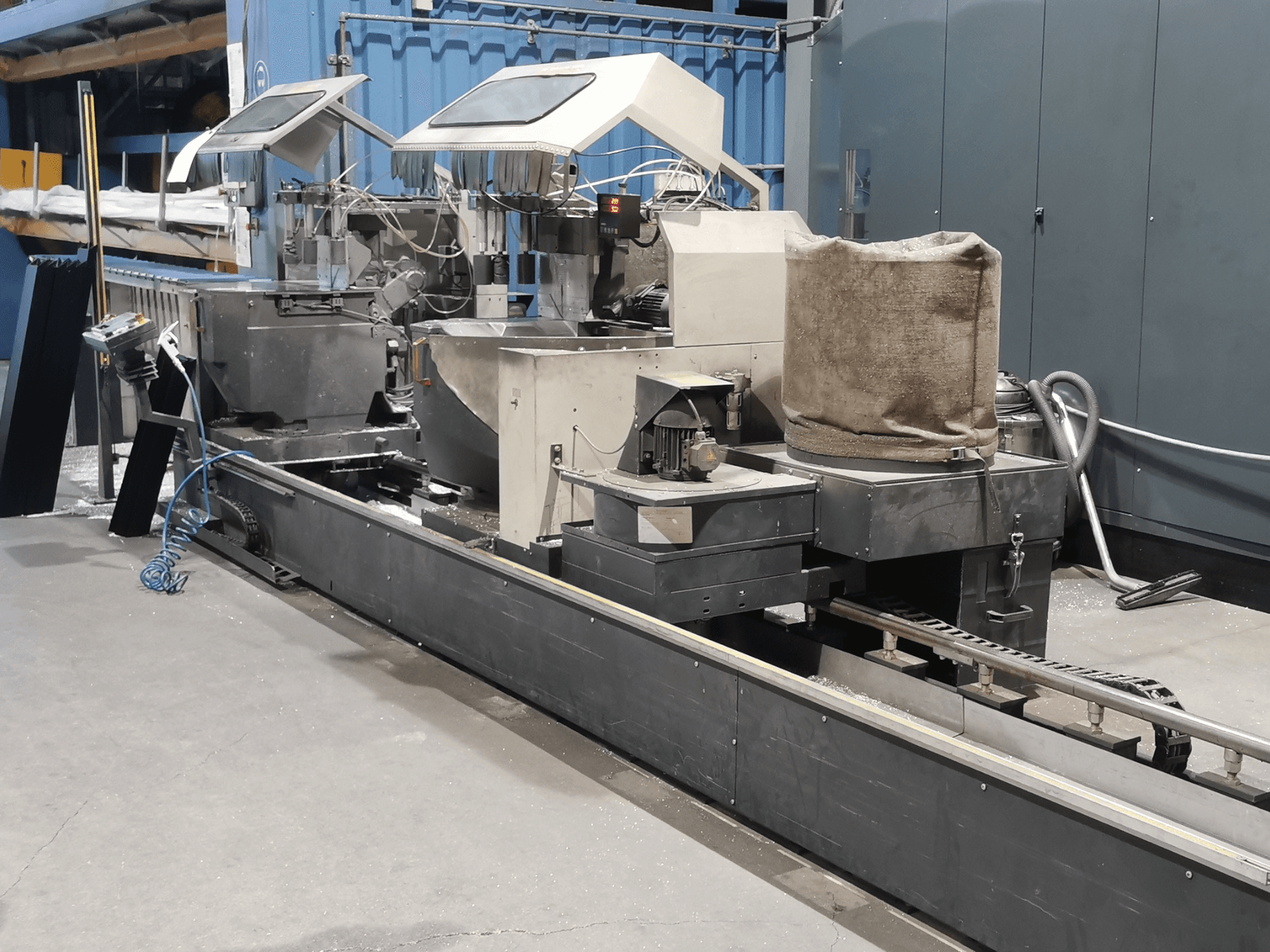 Industrial processing machine viewed from the side, featuring hoppers, conveyor belt, and control panel, in a factory setting.