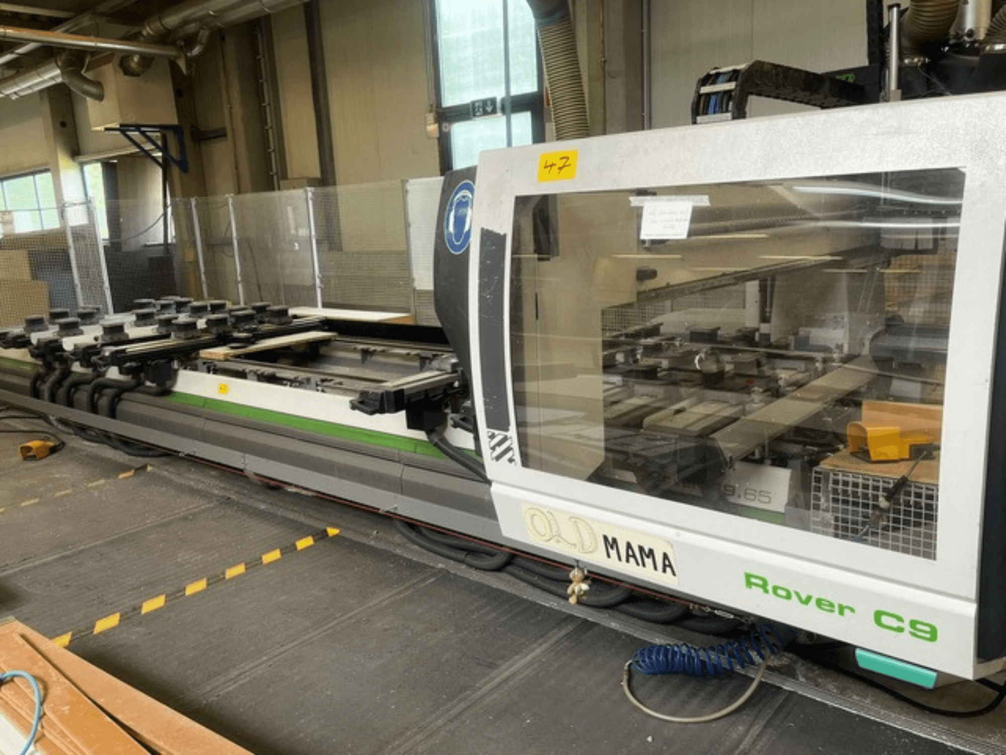 BIESSE Rover C 9.65 CNC router in a workshop, side view showing control panel and worktable with clamps.