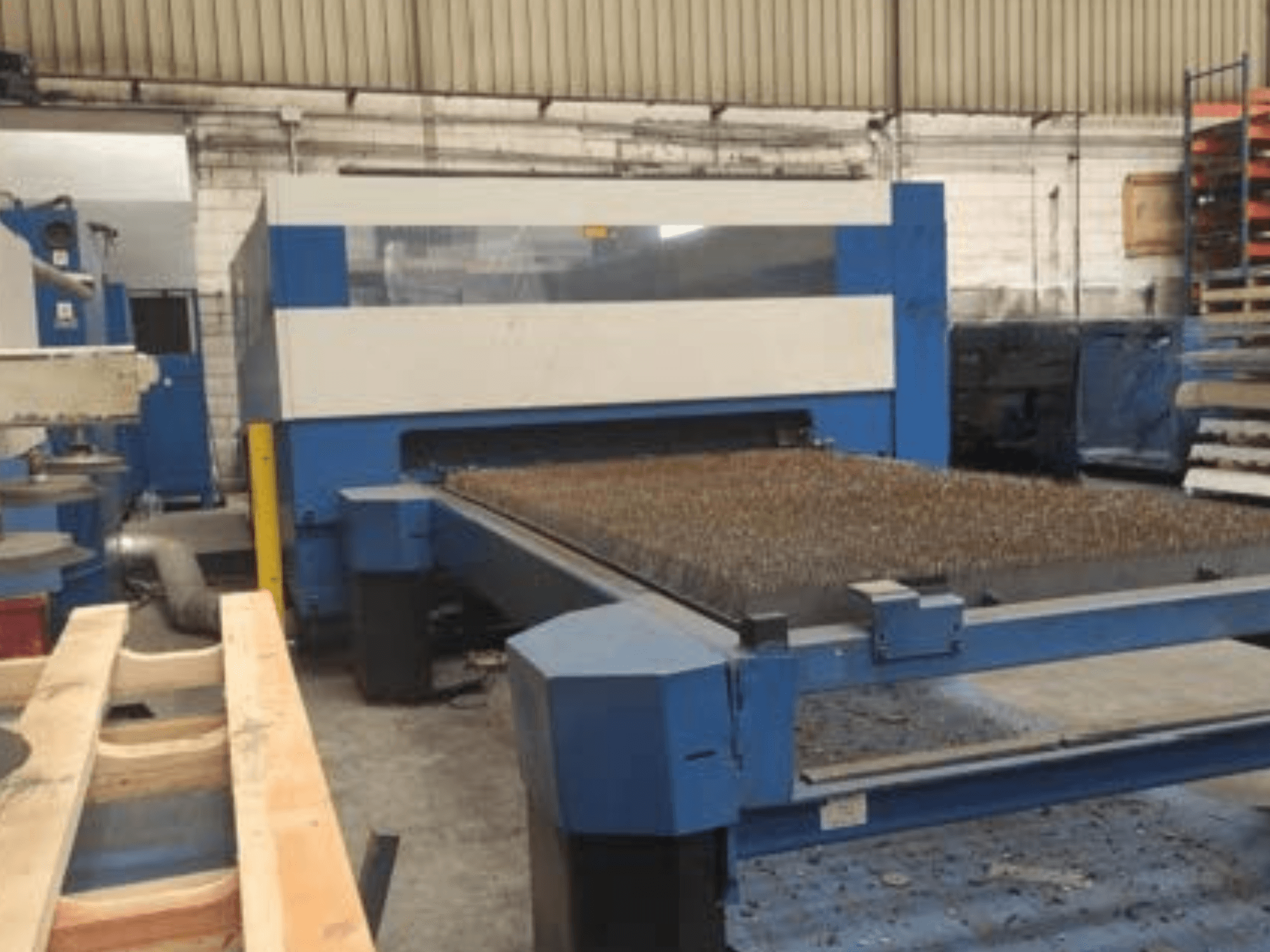 Blue laser cutting machine with a textured metal bed, side view, showing operational setup in an industrial workspace.