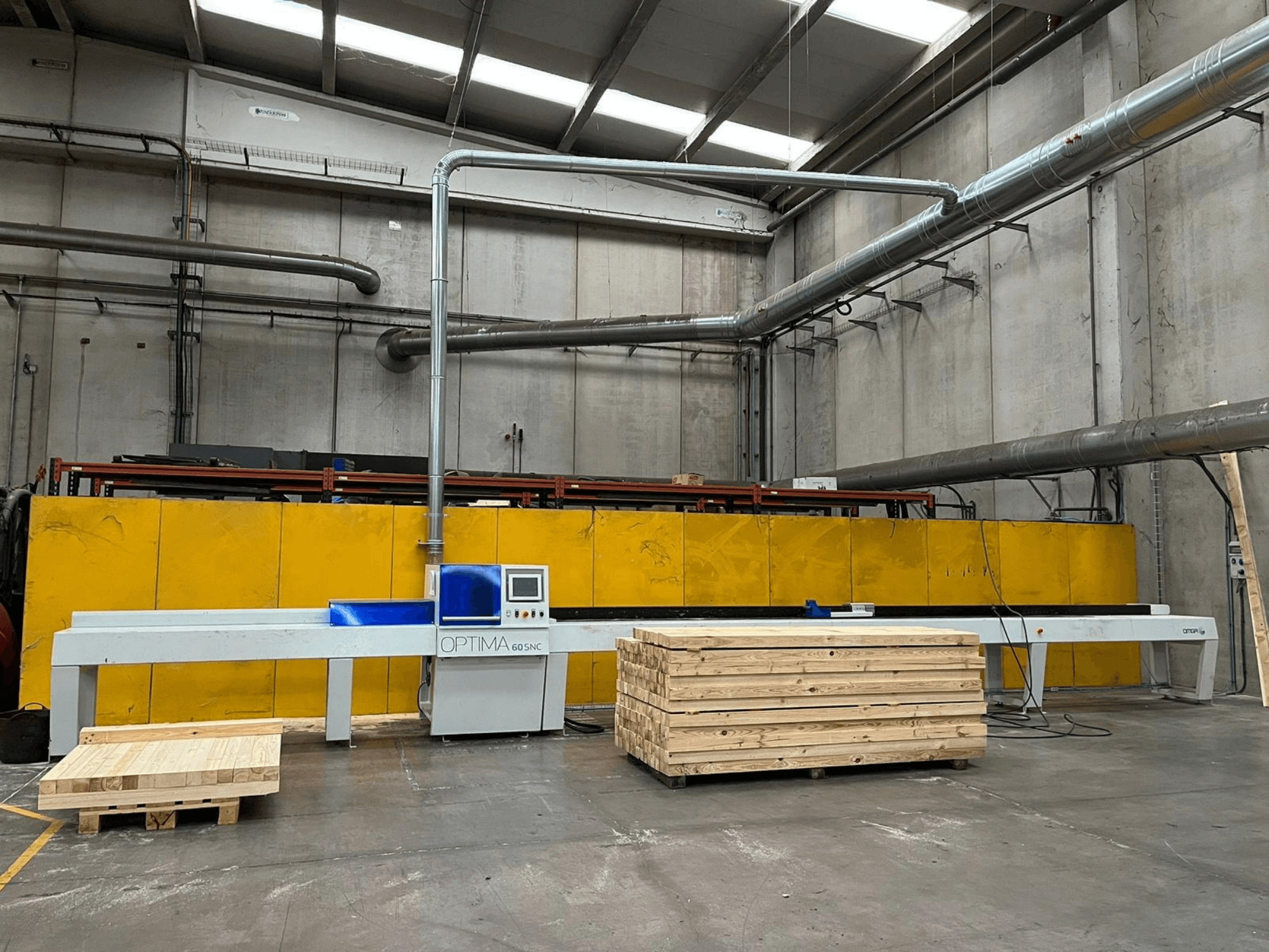 Front view of OPTIMA 60SNC 6200 CE optimizing cross-cut saw, with wooden pallets and yellow safety barriers in the background.